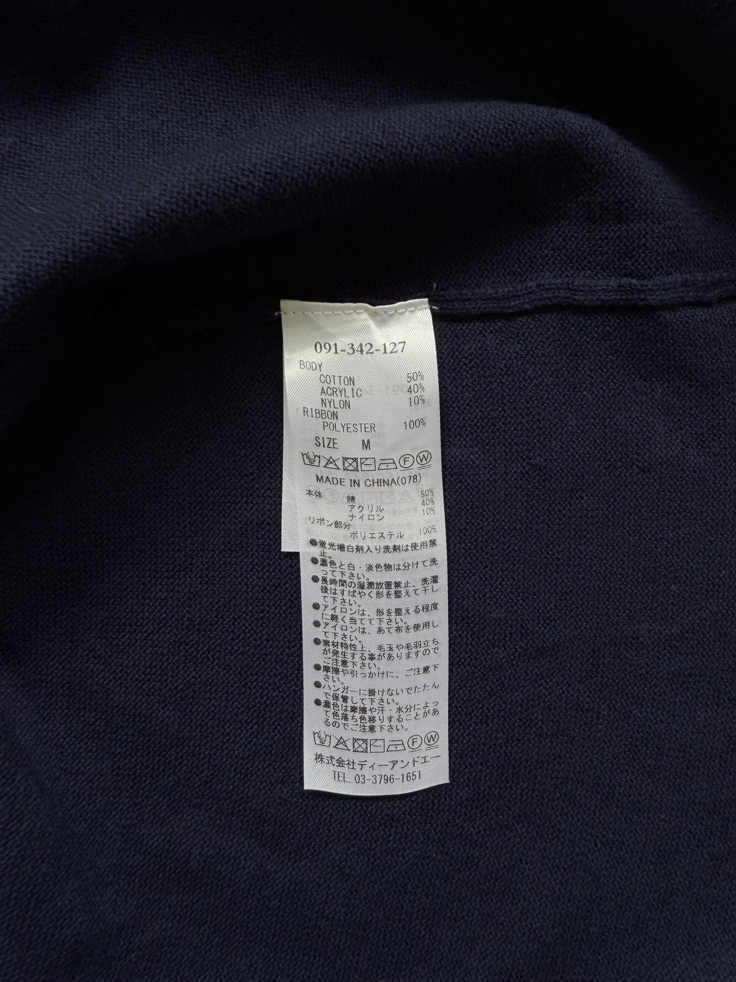Close-up of a dark navy knit garment with a white interior care label sewn onto the inside neck area.