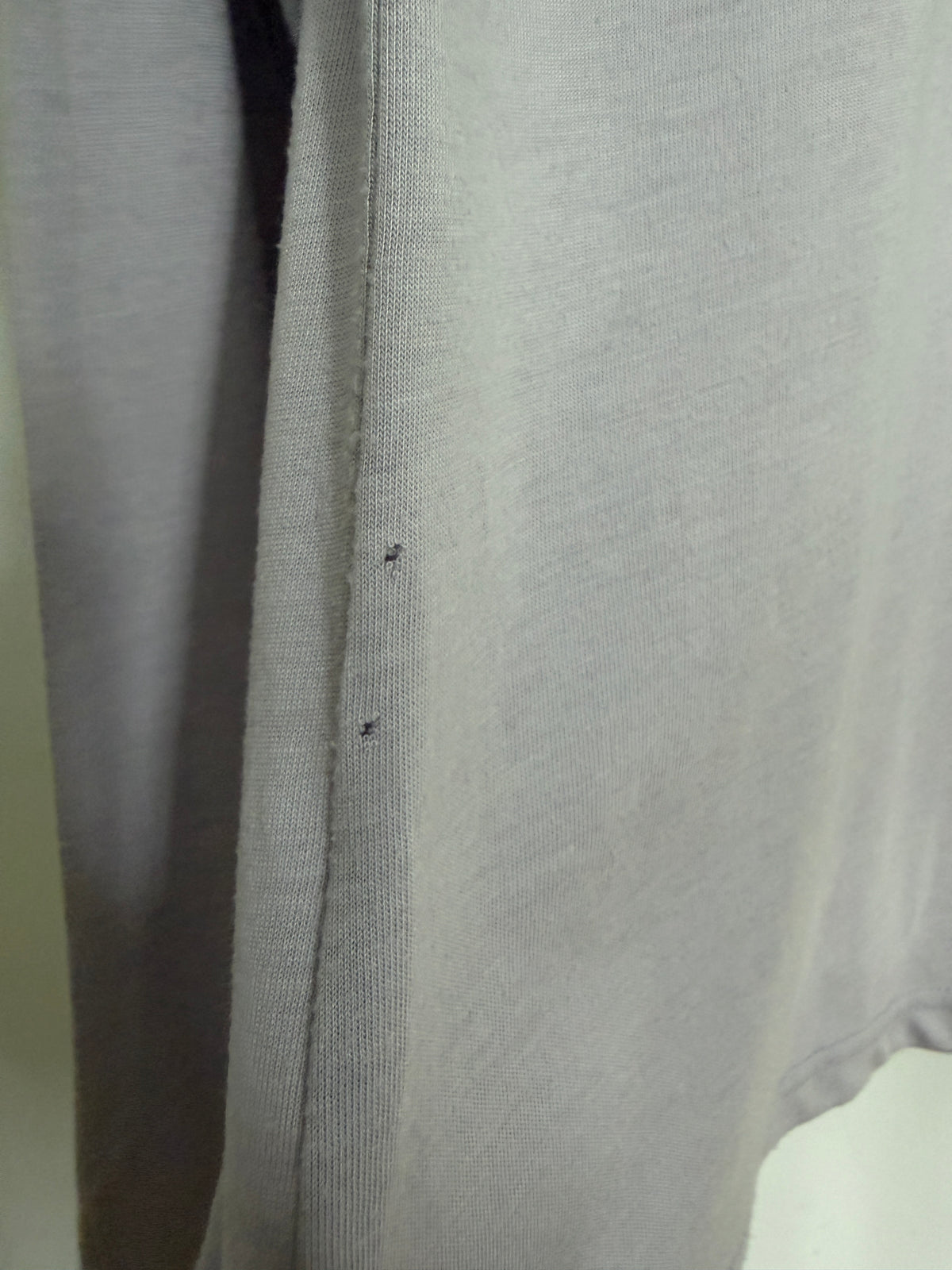 Close-up of a light gray knit fabric garment, showing the texture and a small dark defect or stain on the side seam.
