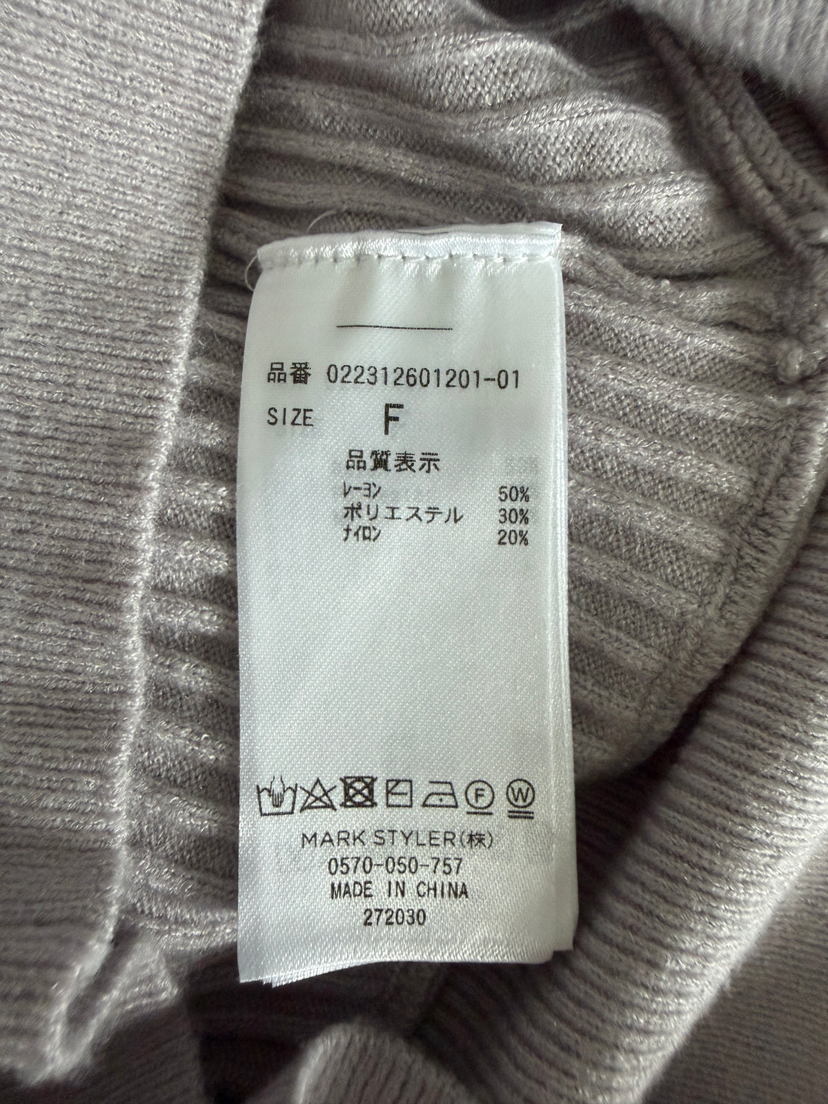 Close-up of a white garment care label sewn onto the inside neck of a ribbed gray knit sweater, showing size F and care symbols.