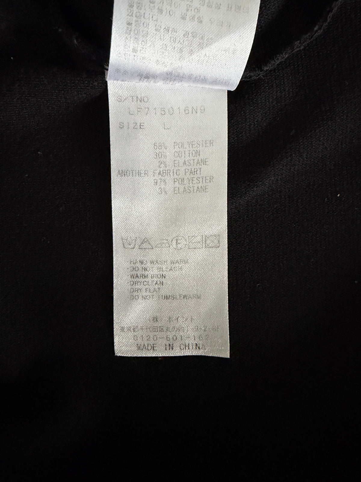 A close-up of a white garment care and size tag sewn onto a black fabric garment. The tag contains printed text with size information and care symbols, including 'MADE IN CHINA'.