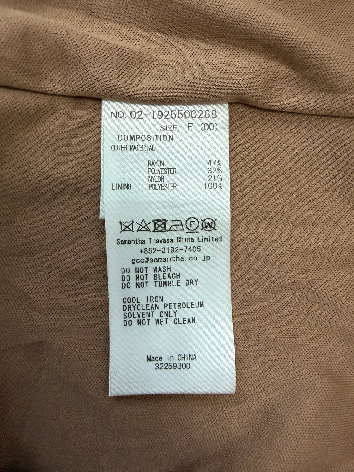 A close-up of a garment's interior label showing composition details, fabric percentages, care symbols, and manufacturer information for Samantha Thavasa China Limited.