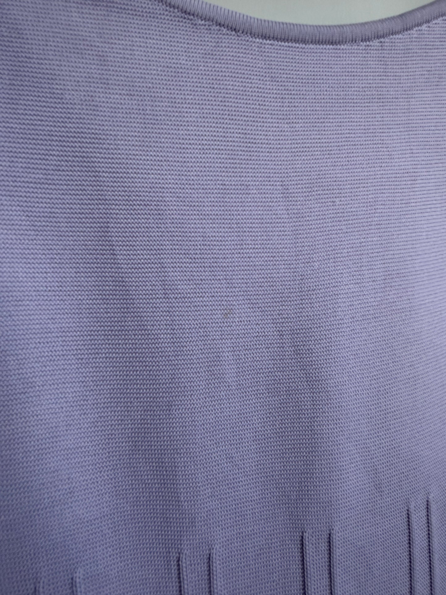 Close-up of a lavender purple knit fabric texture, showing the fine woven pattern and a small portion of a vertical slit neckline.