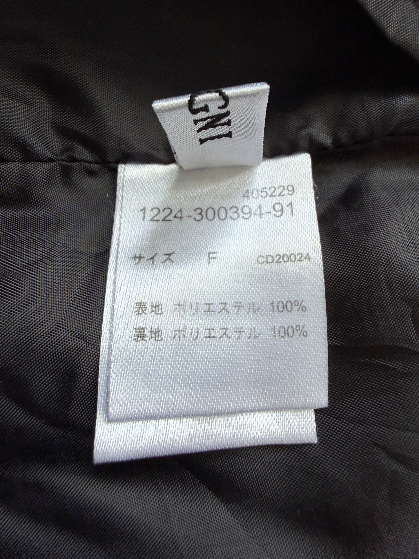 Close-up of a garment's interior tag showing size information in Japanese, with a black quilted fabric background.