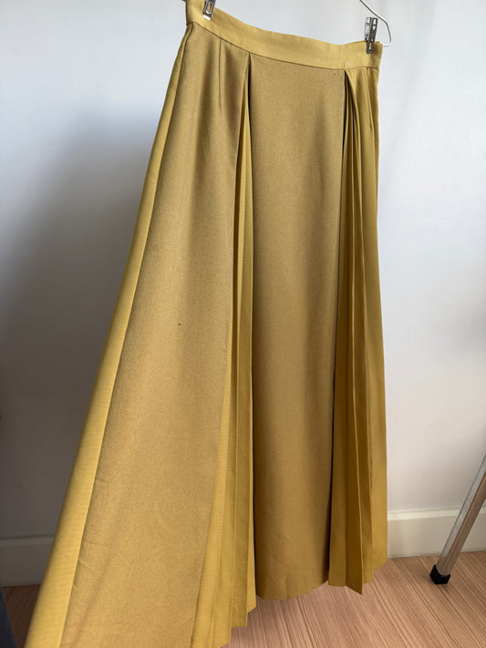 A pleated midi skirt in a mustard yellow color, hanging from a metal hanger against a plain white wall.