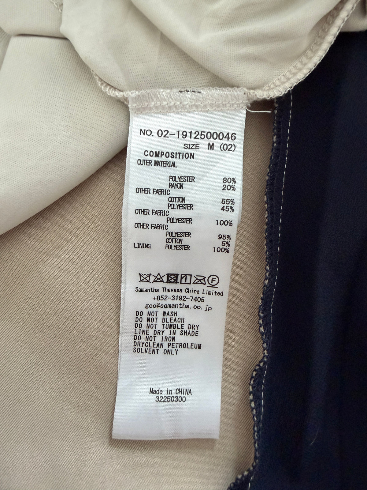 A close-up of a garment's interior label showing composition details, with visible fabric in beige and dark navy colors.