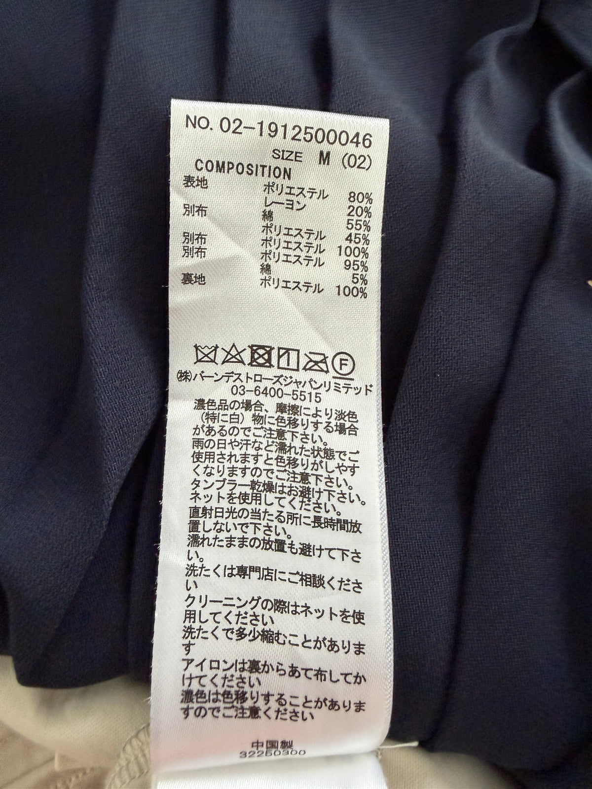 A close-up of a white garment care label with Japanese text and composition details, placed against dark navy fabric.