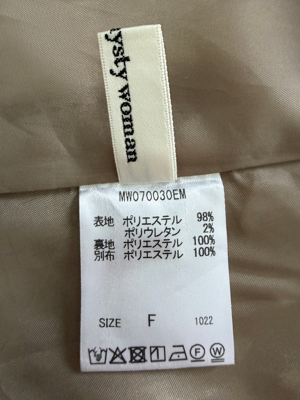 Close-up of a garment's interior labels showing a cream-colored brand tag reading 'systy woman' and a white material composition tag with Japanese text and care symbols.