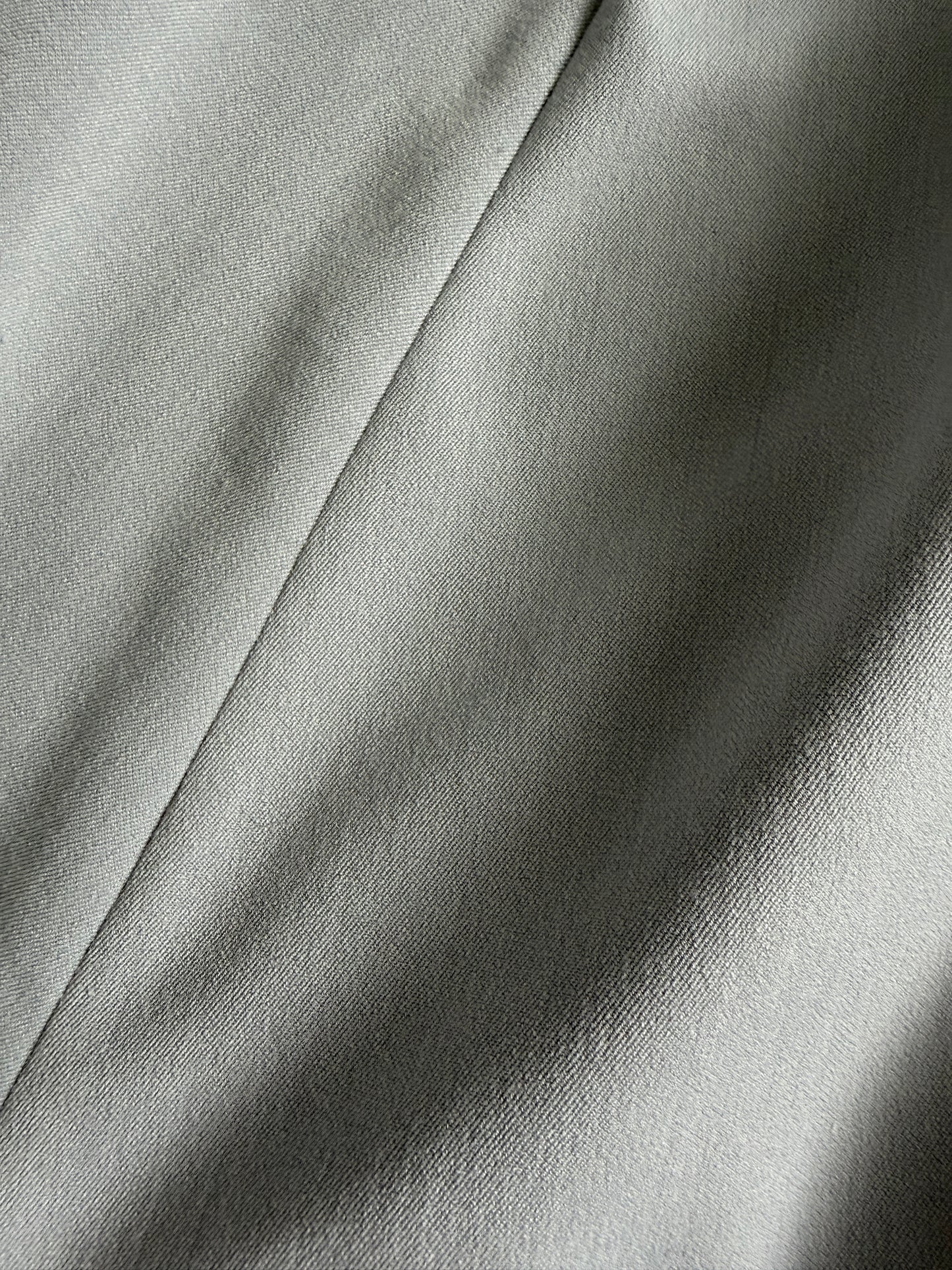A close-up of draped light gray fabric with soft folds and a subtle woven texture.