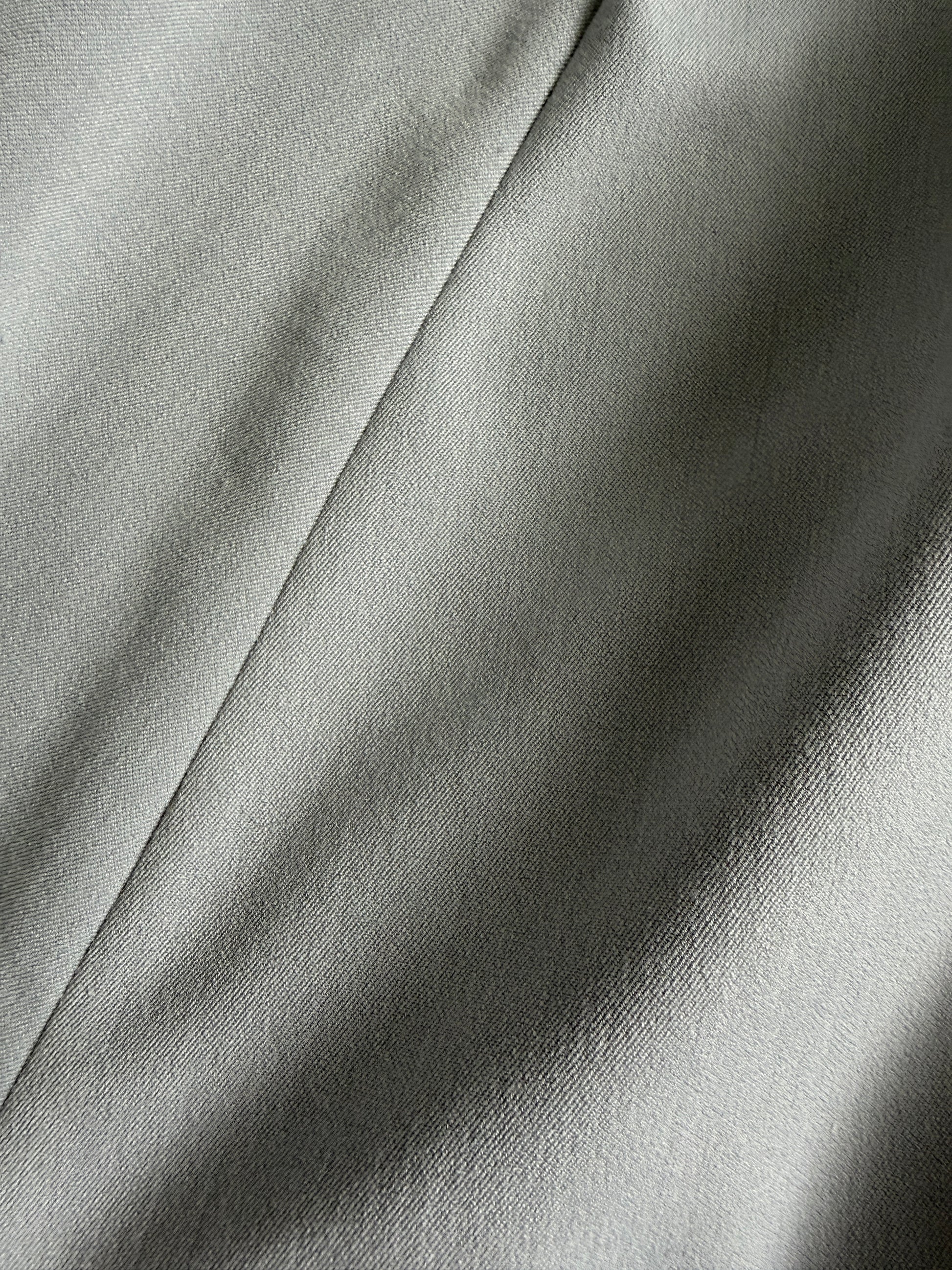 A close-up of draped light gray fabric with soft folds and a subtle woven texture.