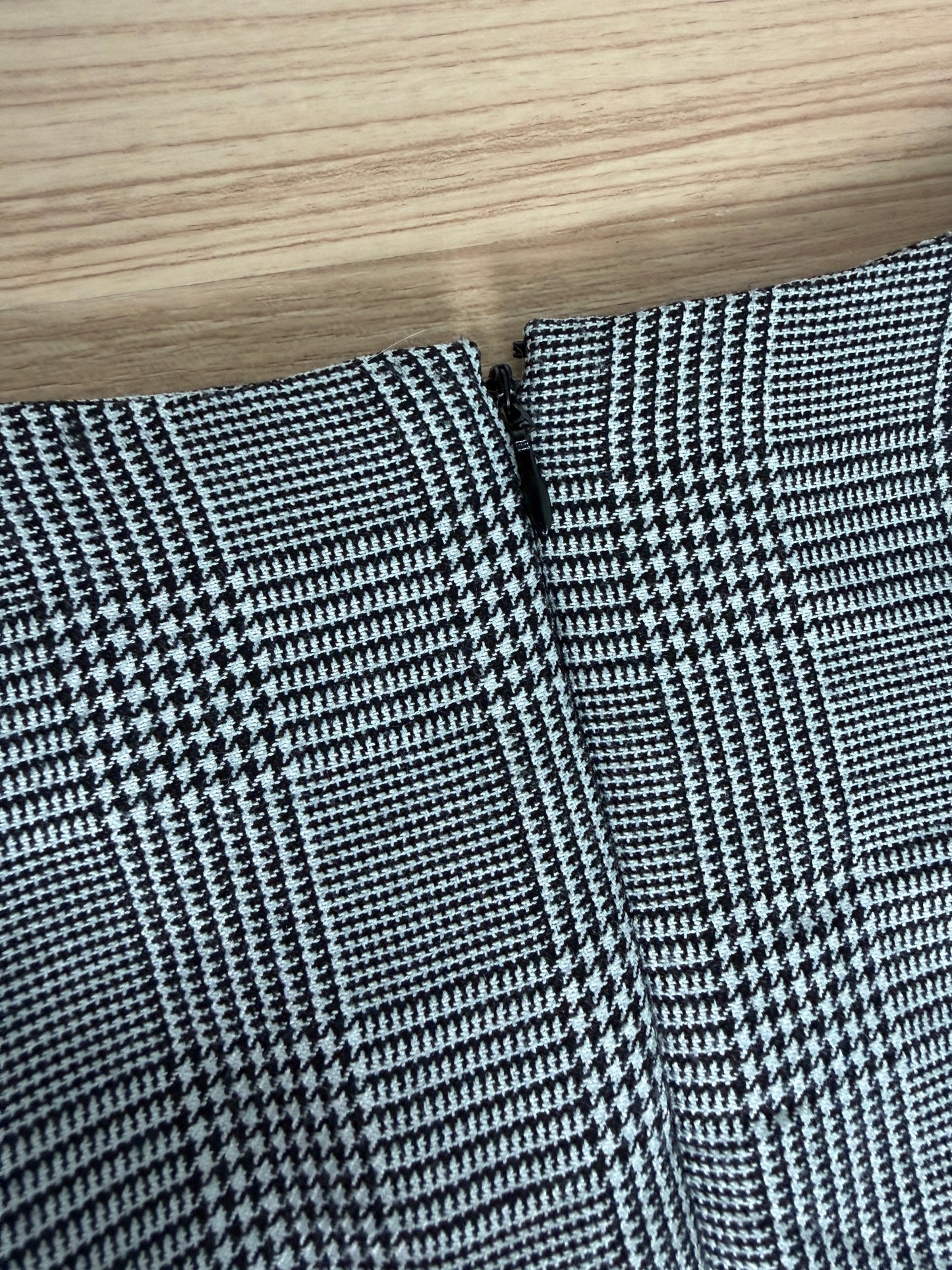 Close-up of a black and white houndstooth patterned fabric, showing the texture and fold details, with a light wood grain surface visible at the top.