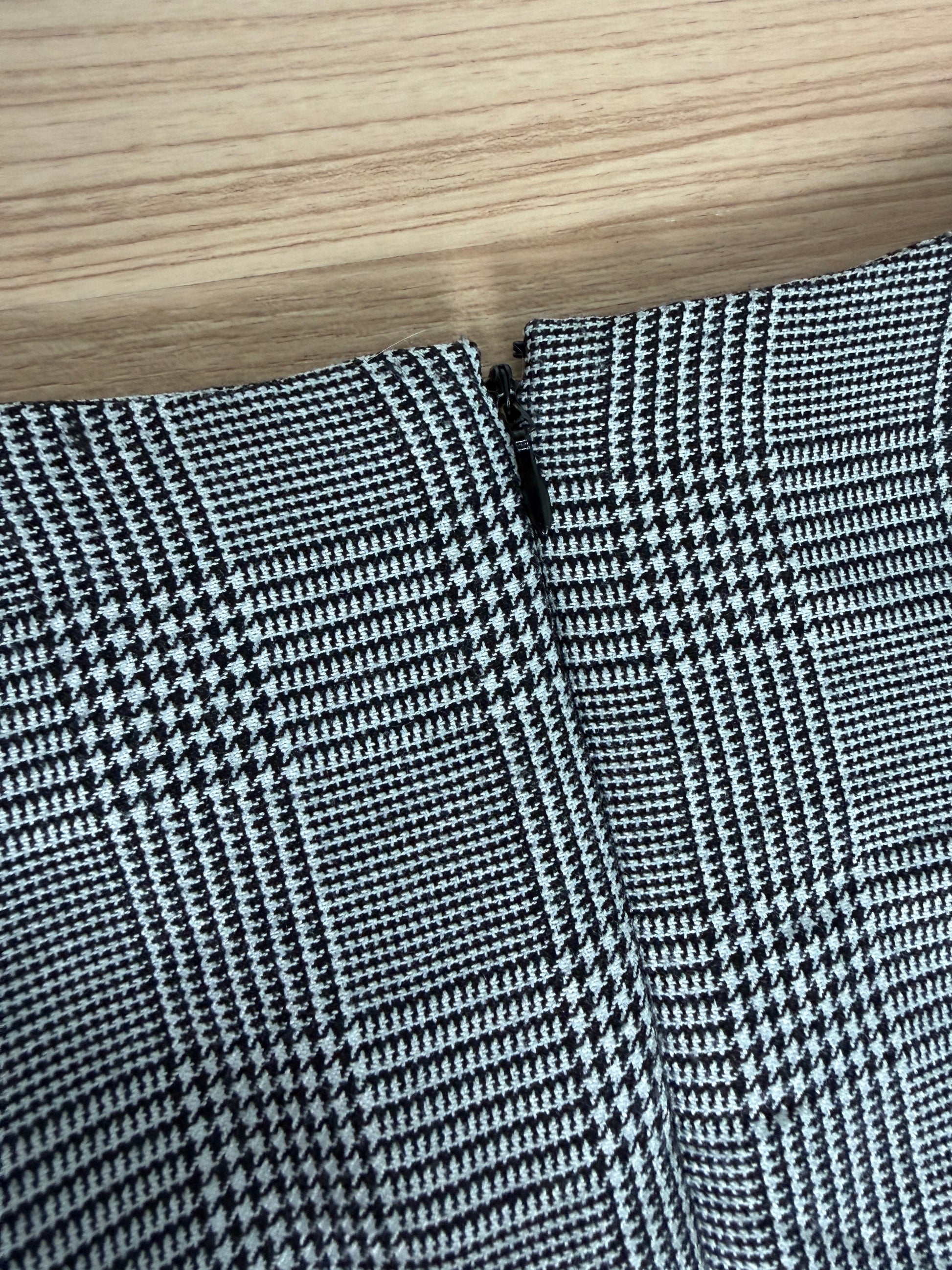 Close-up of a black and white houndstooth patterned fabric, showing the texture and fold details, with a light wood grain surface visible at the top.