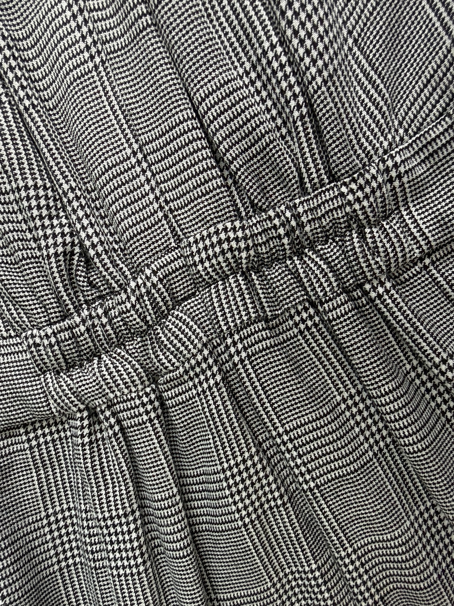 Close-up of a black and white micro-check patterned fabric with gathered pleats and a tie detail.