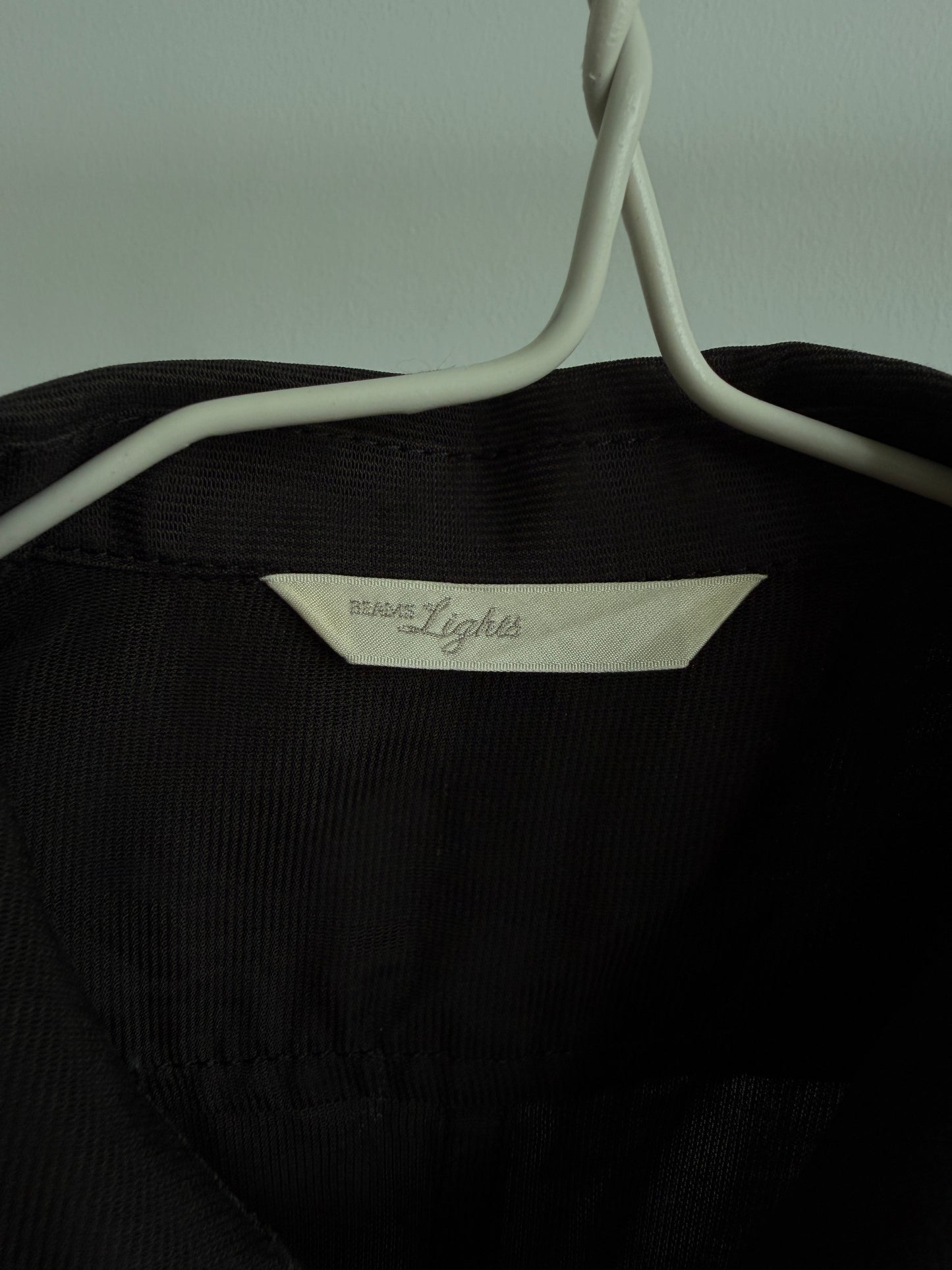 Close-up of a black ribbed garment hanging on a white hanger, showing a cream fabric label that reads 'BEAMS LIGHTS'.