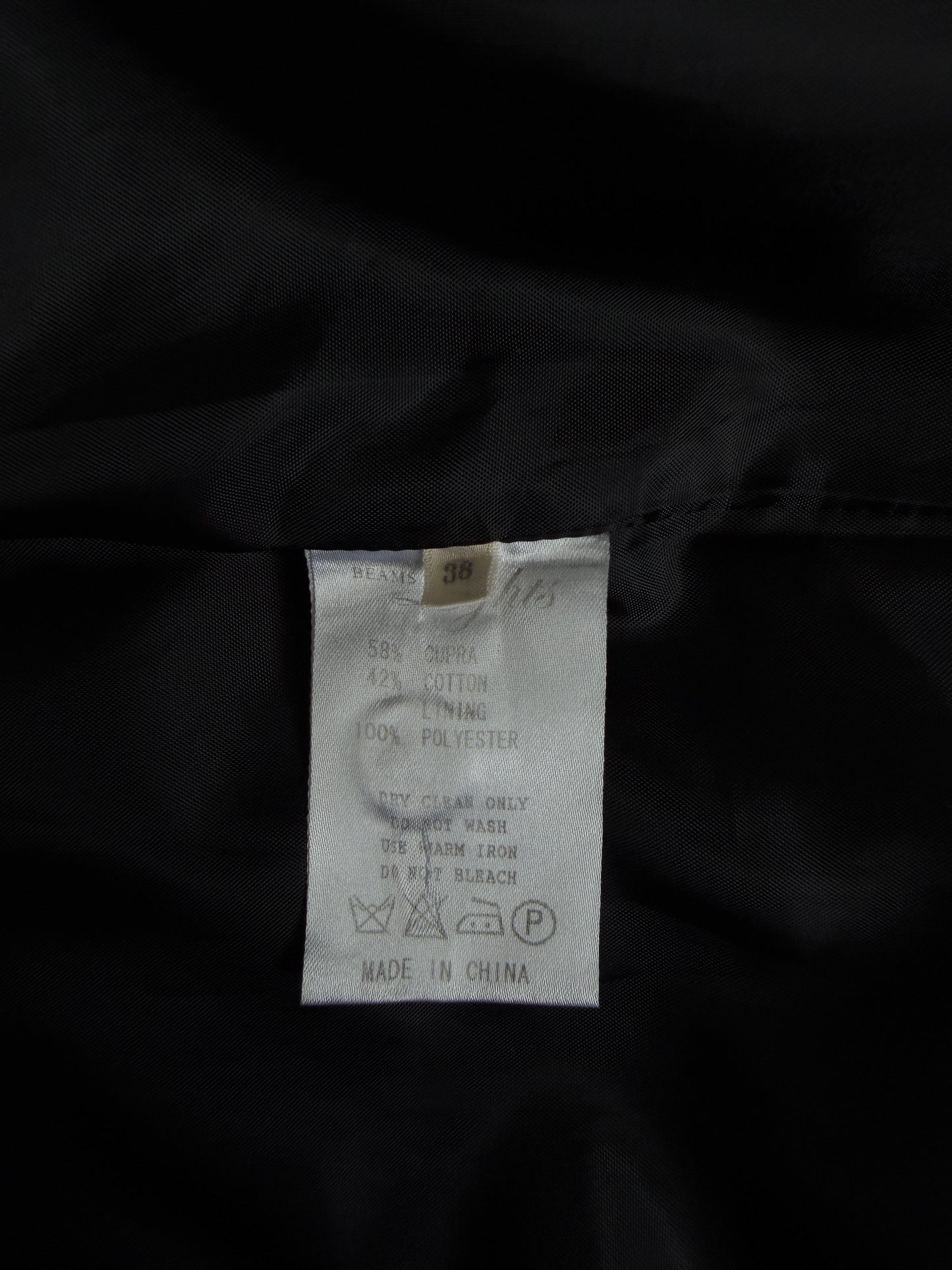 Close-up of a garment's interior label sewn onto black fabric, showing a white care tag with text and washing symbols.