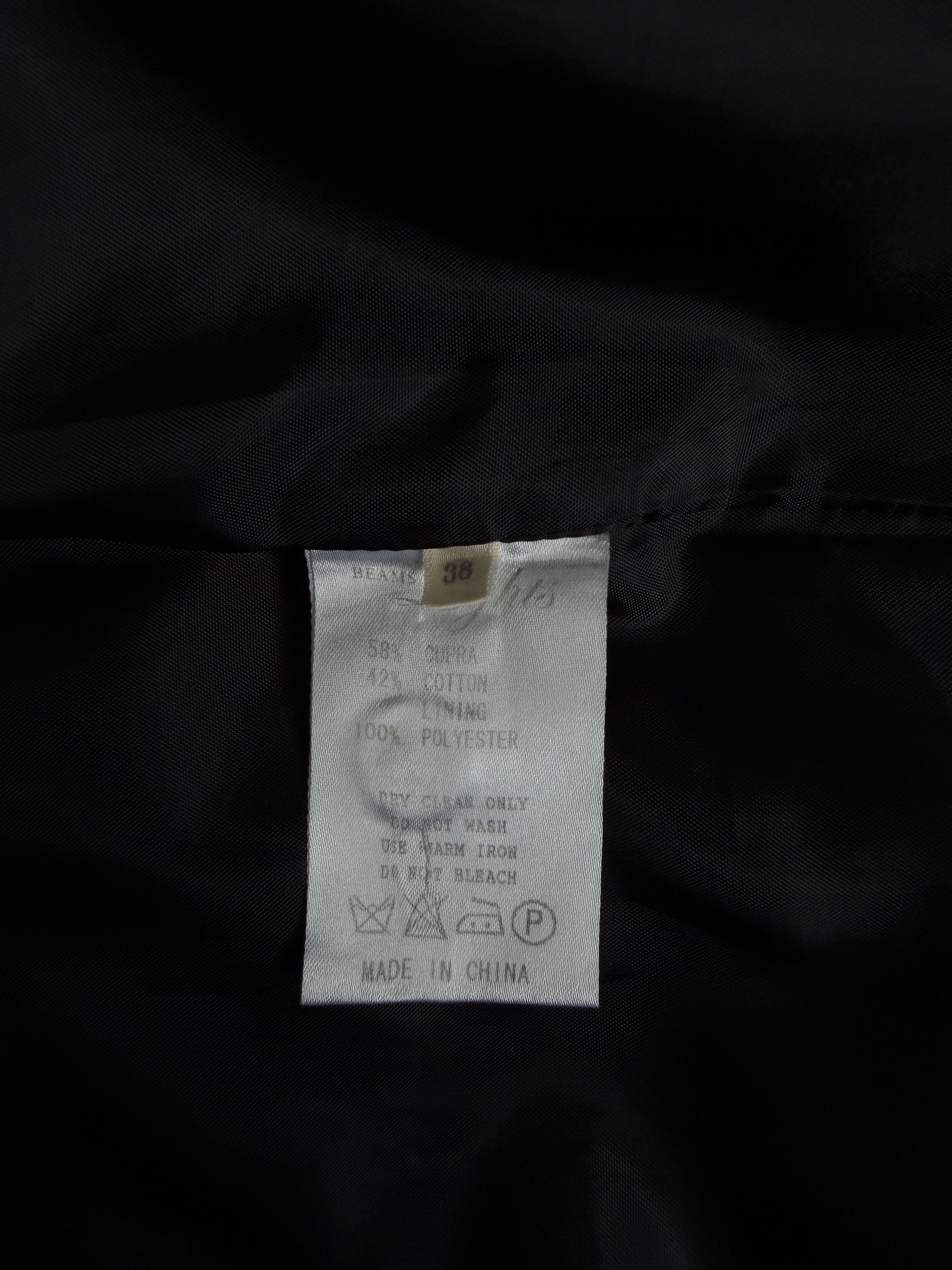 Close-up of a garment's interior label sewn onto black fabric, showing a white care tag with text and washing symbols.