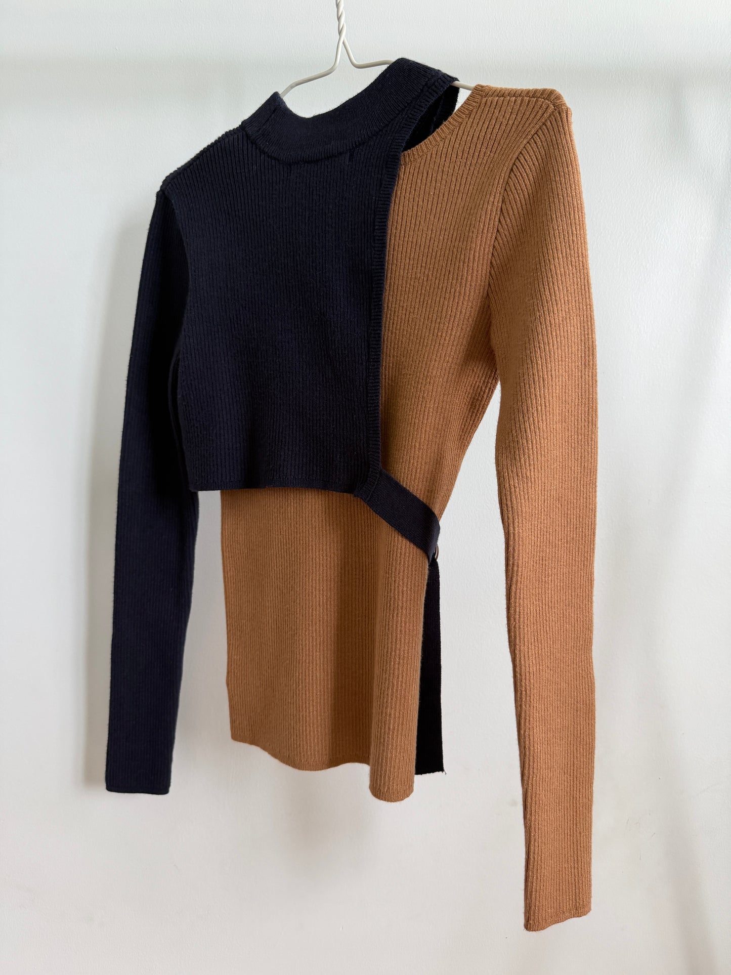A color-block ribbed knit long-sleeve top hanging on a white hanger against a plain white background. The top features a dark navy blue front panel and sleeves, with a warm camel brown front panel and side wrap detail.