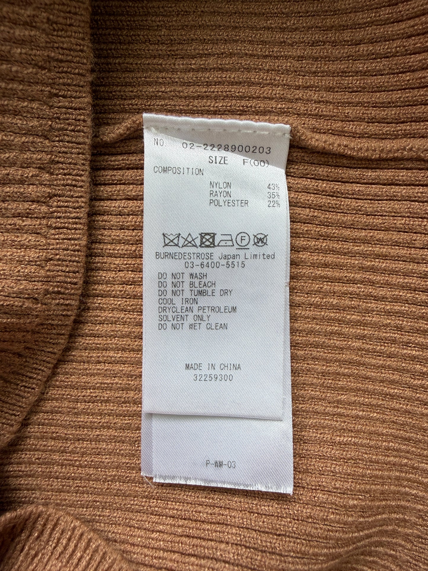 A close-up of a white garment size and composition label sewn onto brown ribbed knit fabric.