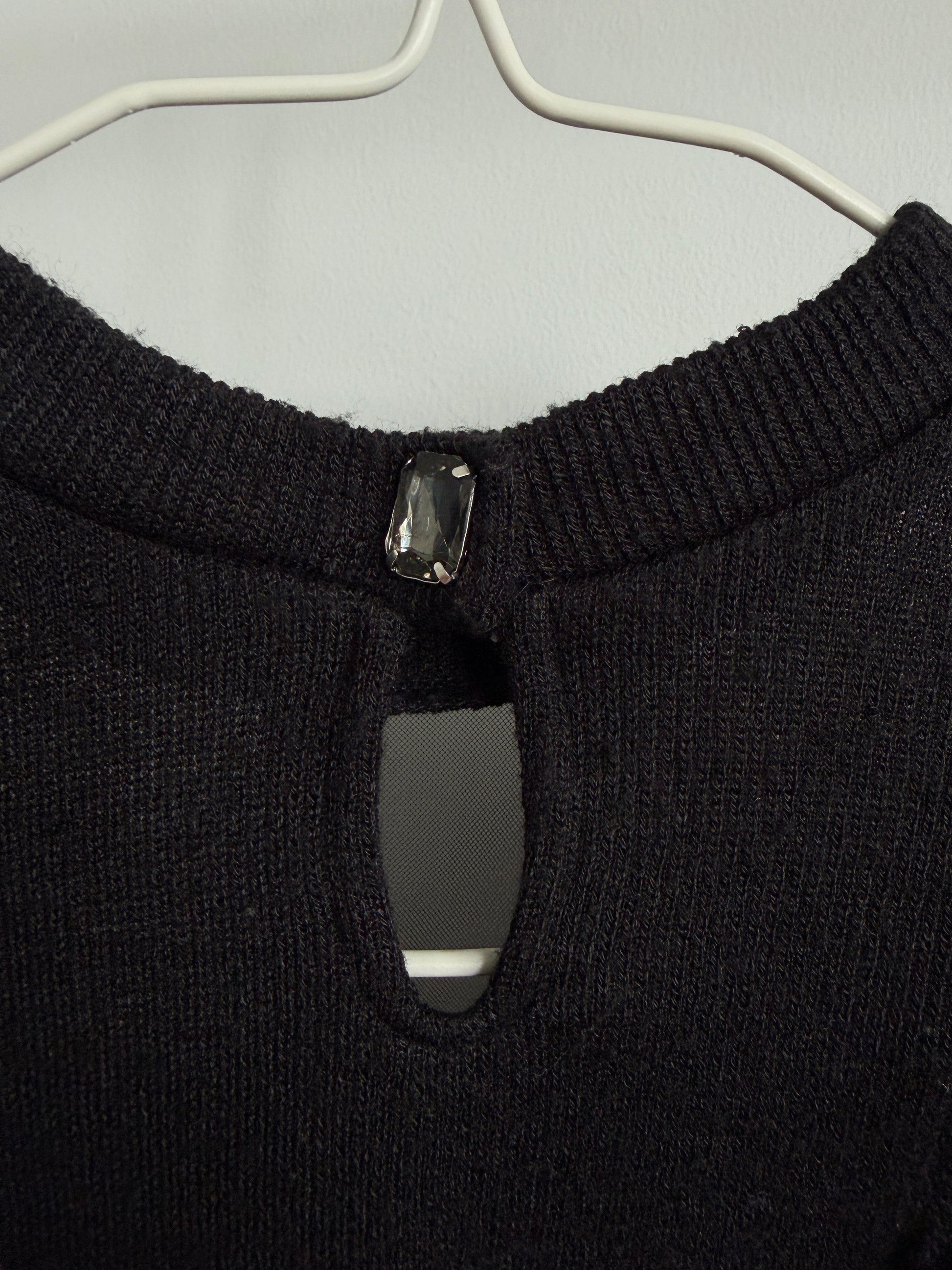 Close-up of a black knit sweater on a white hanger, showing a keyhole cutout at the neckline with a dark rectangular jewel detail.
