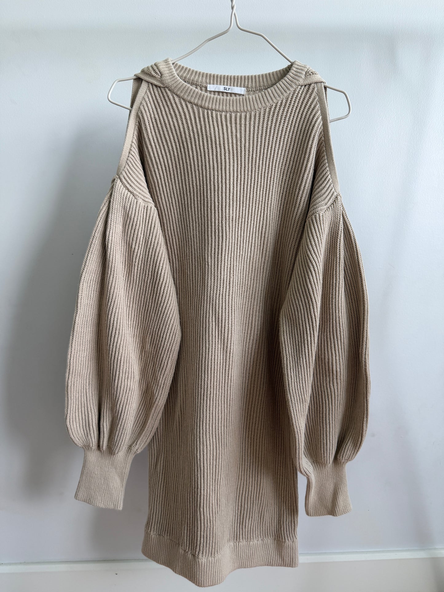 A beige ribbed knit sweater dress with balloon sleeves, hanging on a metal hanger against a plain white wall.
