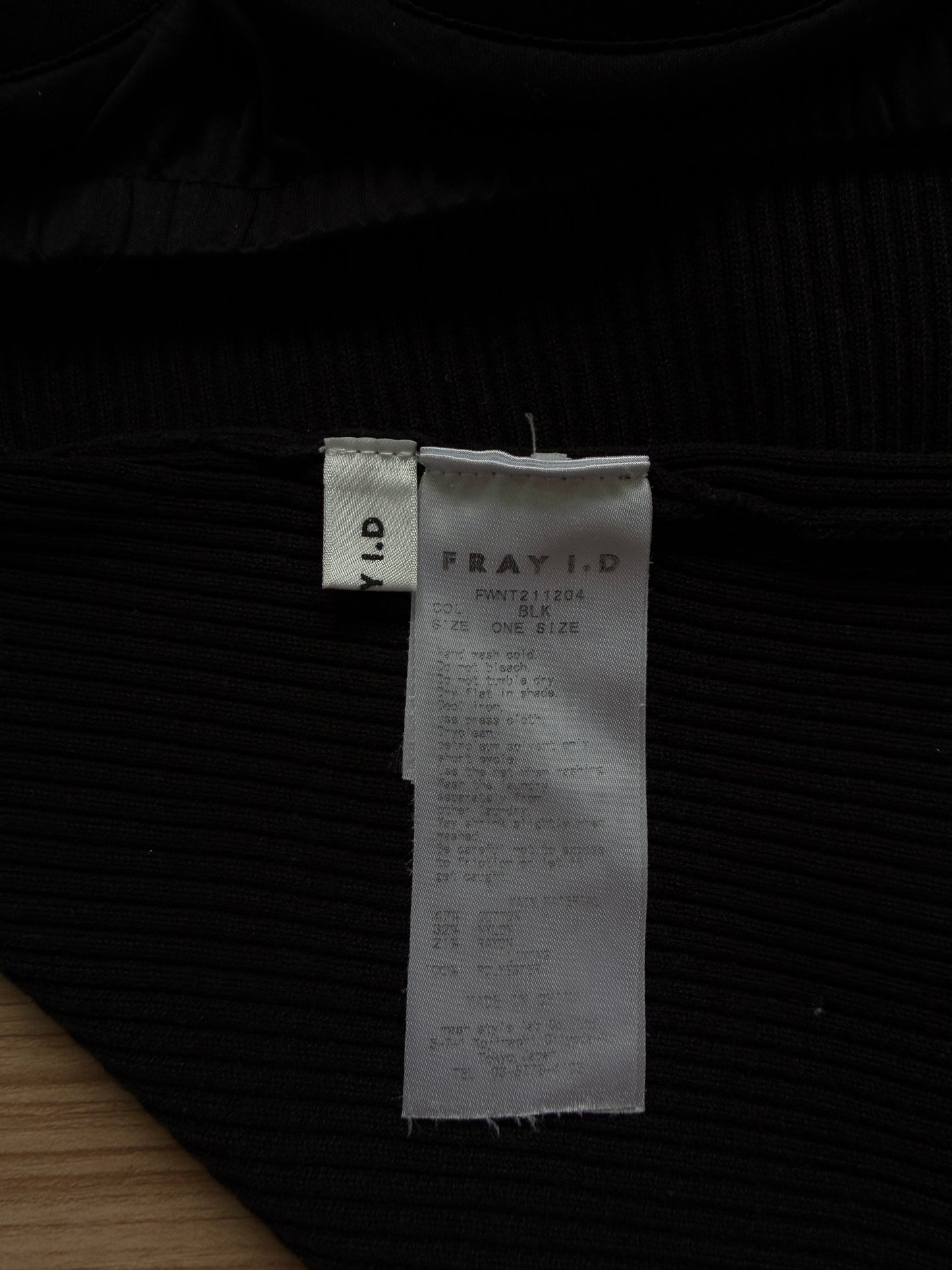 Close-up of a black ribbed knit garment with a white sewn-in size tag reading FRAY ID.