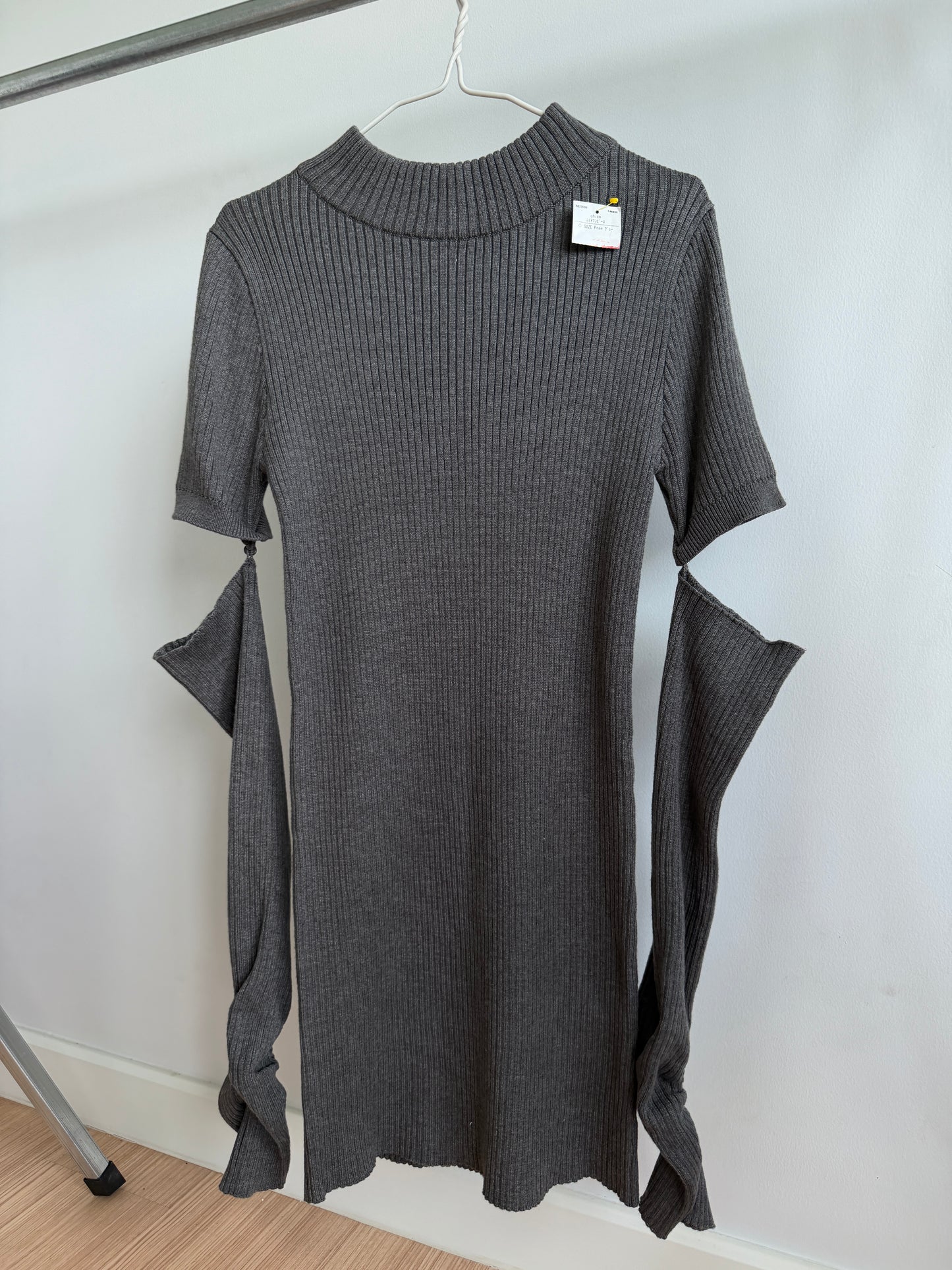 A dark gray ribbed knit short-sleeve dress with unique side cutouts and draped fabric details, hanging on a metal hanger against a white wall.