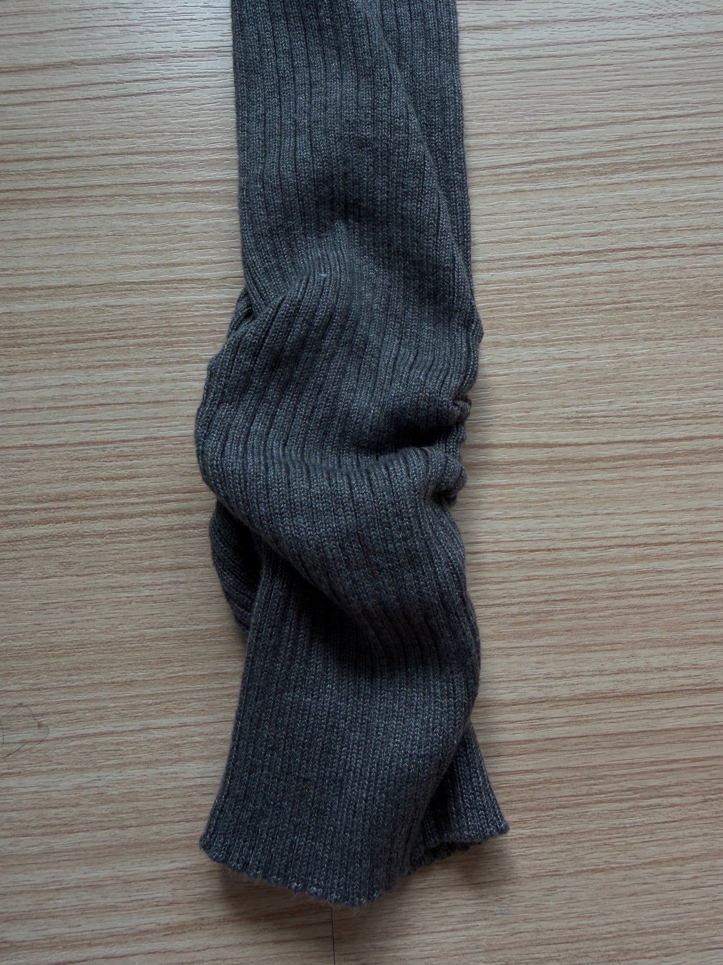 A close-up of a dark gray ribbed knit sleeve or cuff laid on a light wood surface.