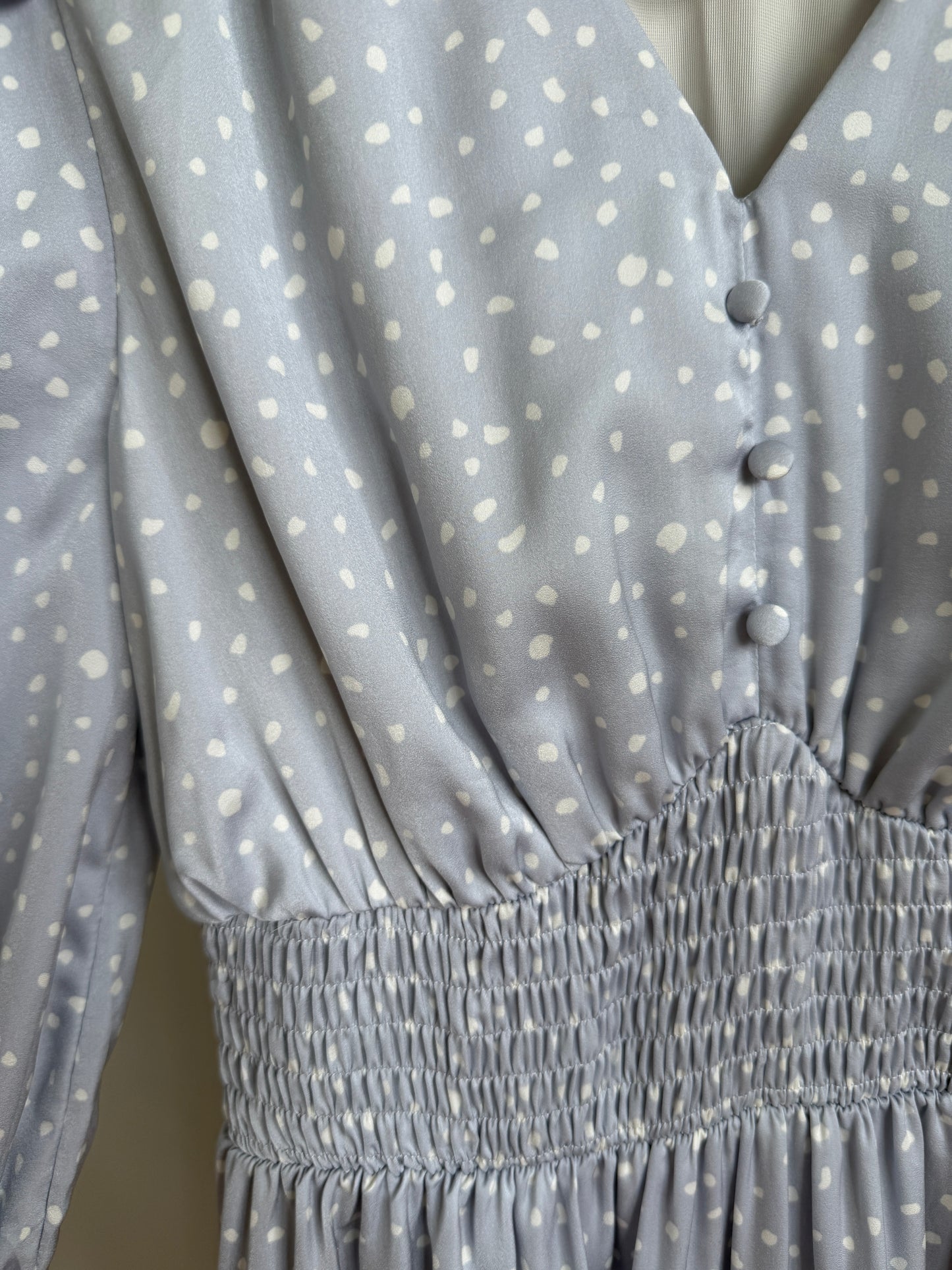 Close-up of a light blue-gray dress with white speckled polka dots, featuring a smocked waist and buttoned neckline.