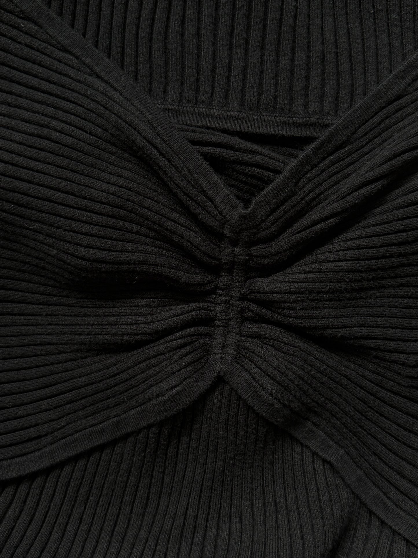 Close-up of a black ribbed knit top with a twisted knot or bow-like gathered detail at the center front.