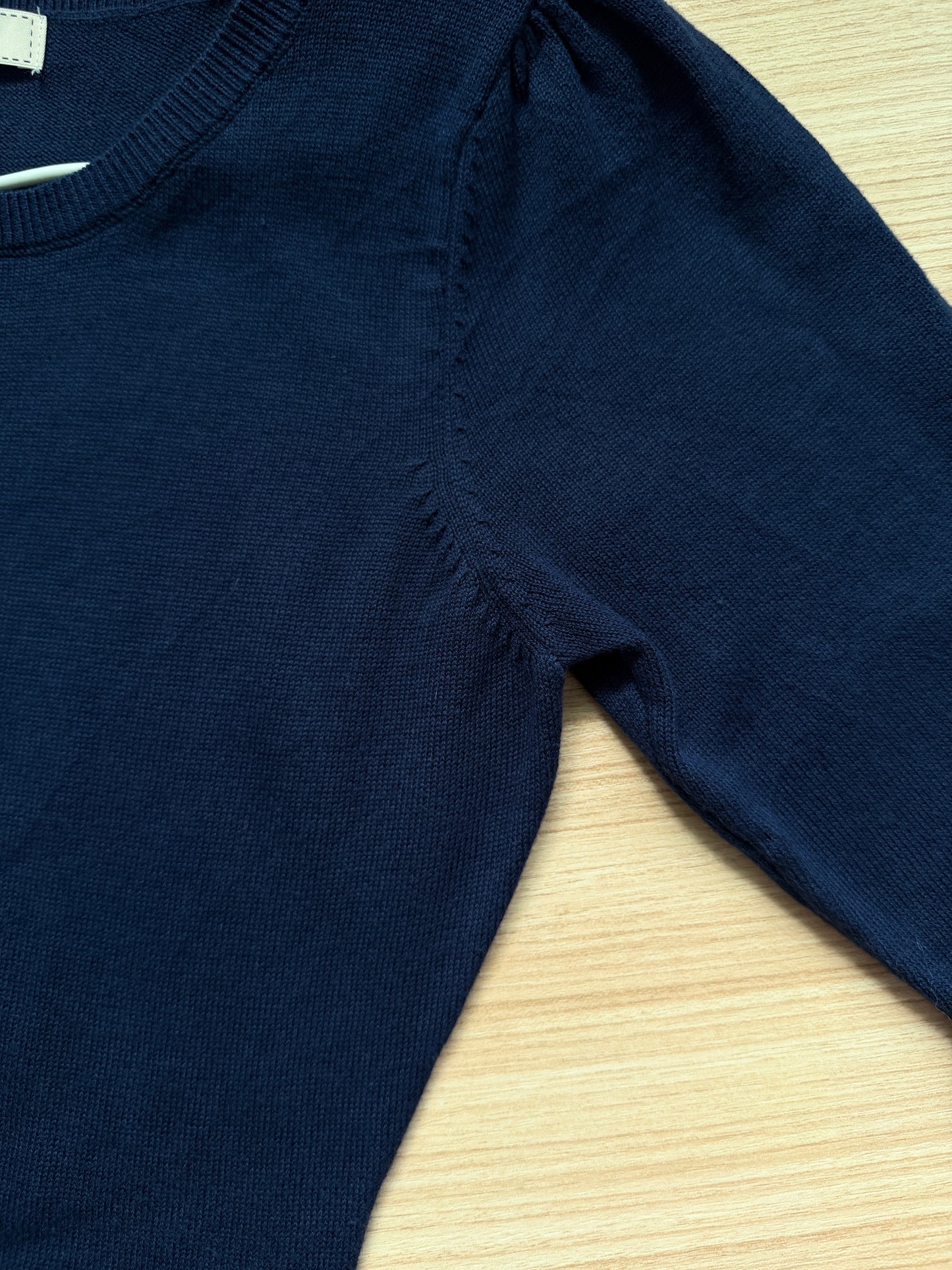 Close-up of a dark navy blue ribbed knit sweater laid flat on a light wood surface, showing the shoulder seam and sleeve.