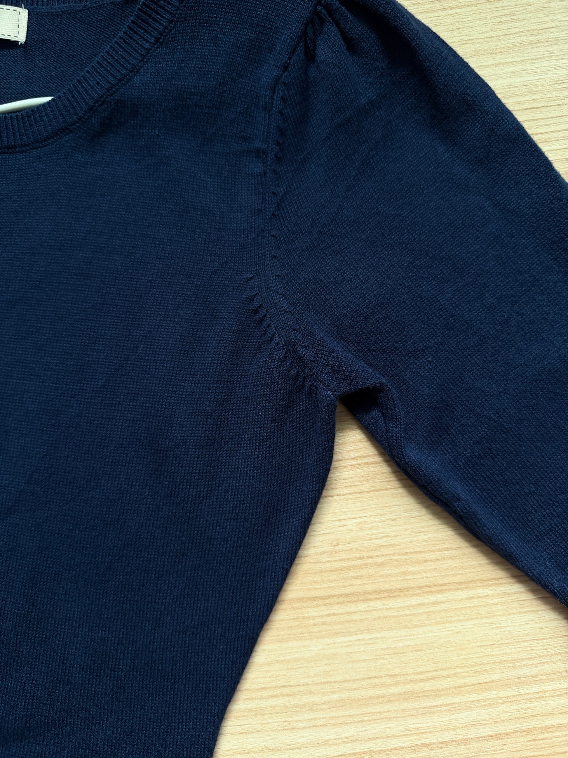 Close-up of a dark navy blue ribbed knit sweater laid flat on a light wood surface, showing the shoulder seam and sleeve.