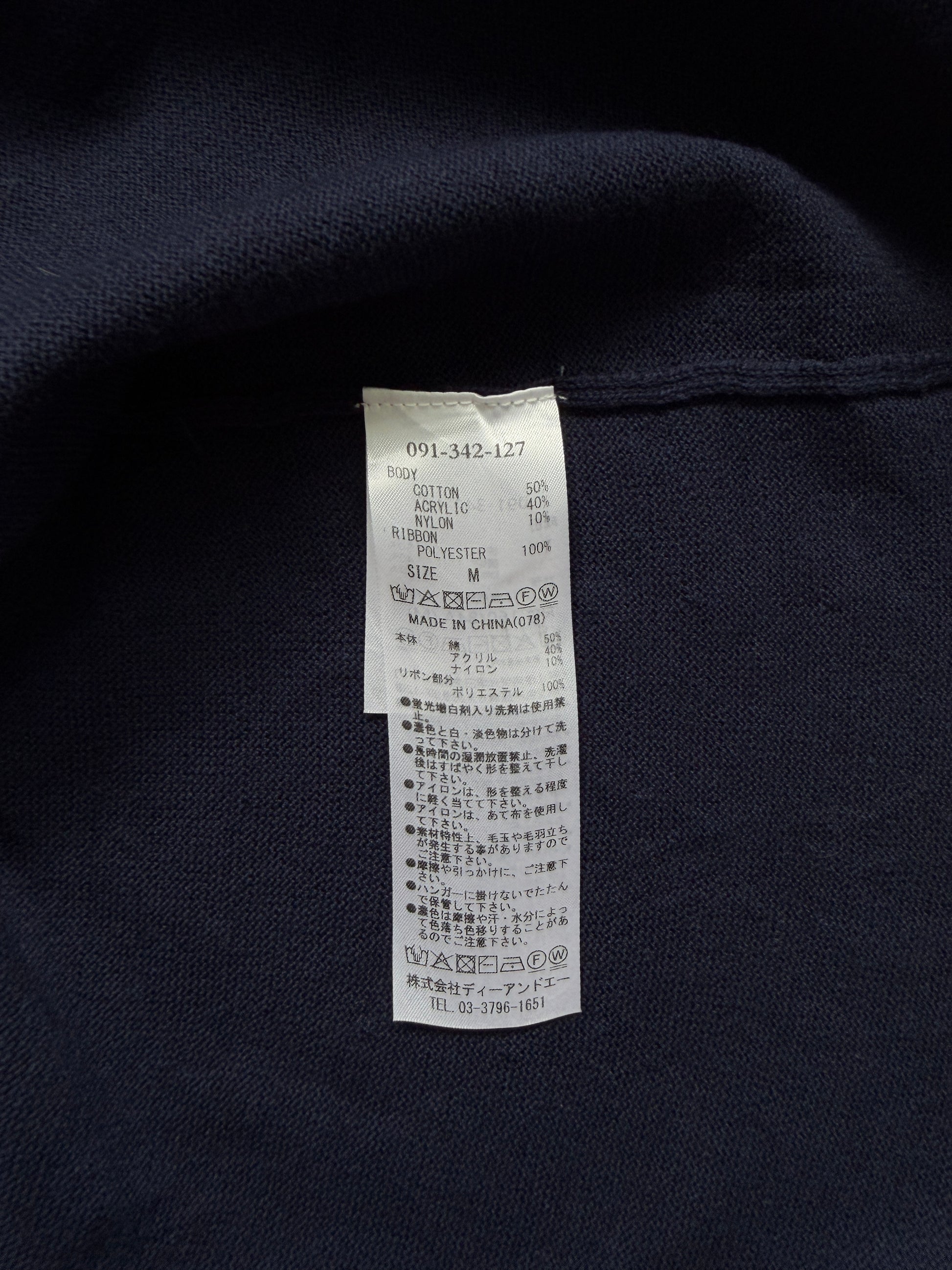 Close-up of a dark navy knit garment with a white interior care label sewn onto the inside neck area.