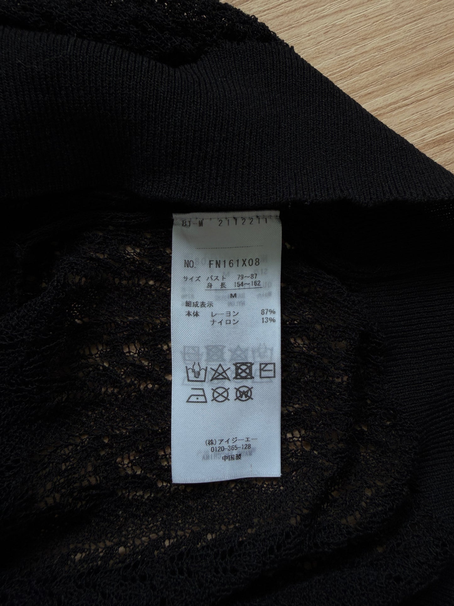 Close-up of a black lace garment showing the interior care label, photographed on a light wood surface.