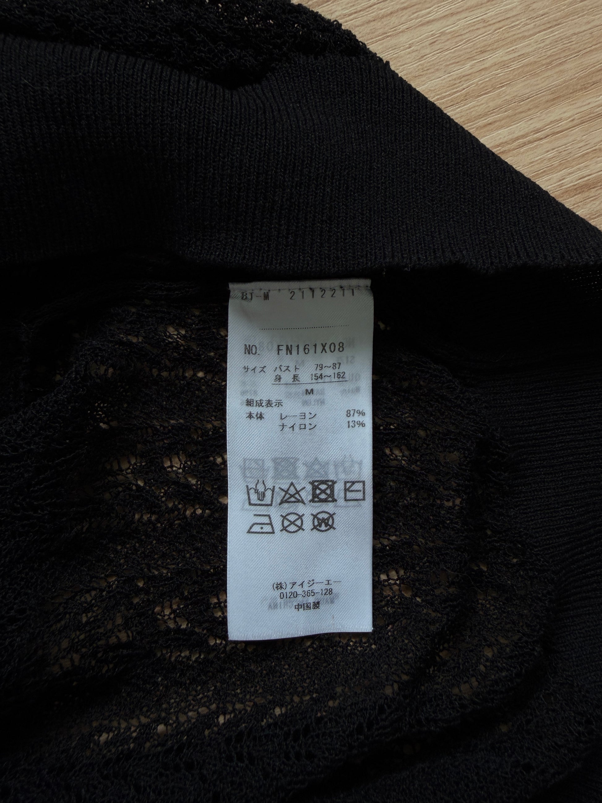 Close-up of a black lace garment showing the interior care label, photographed on a light wood surface.