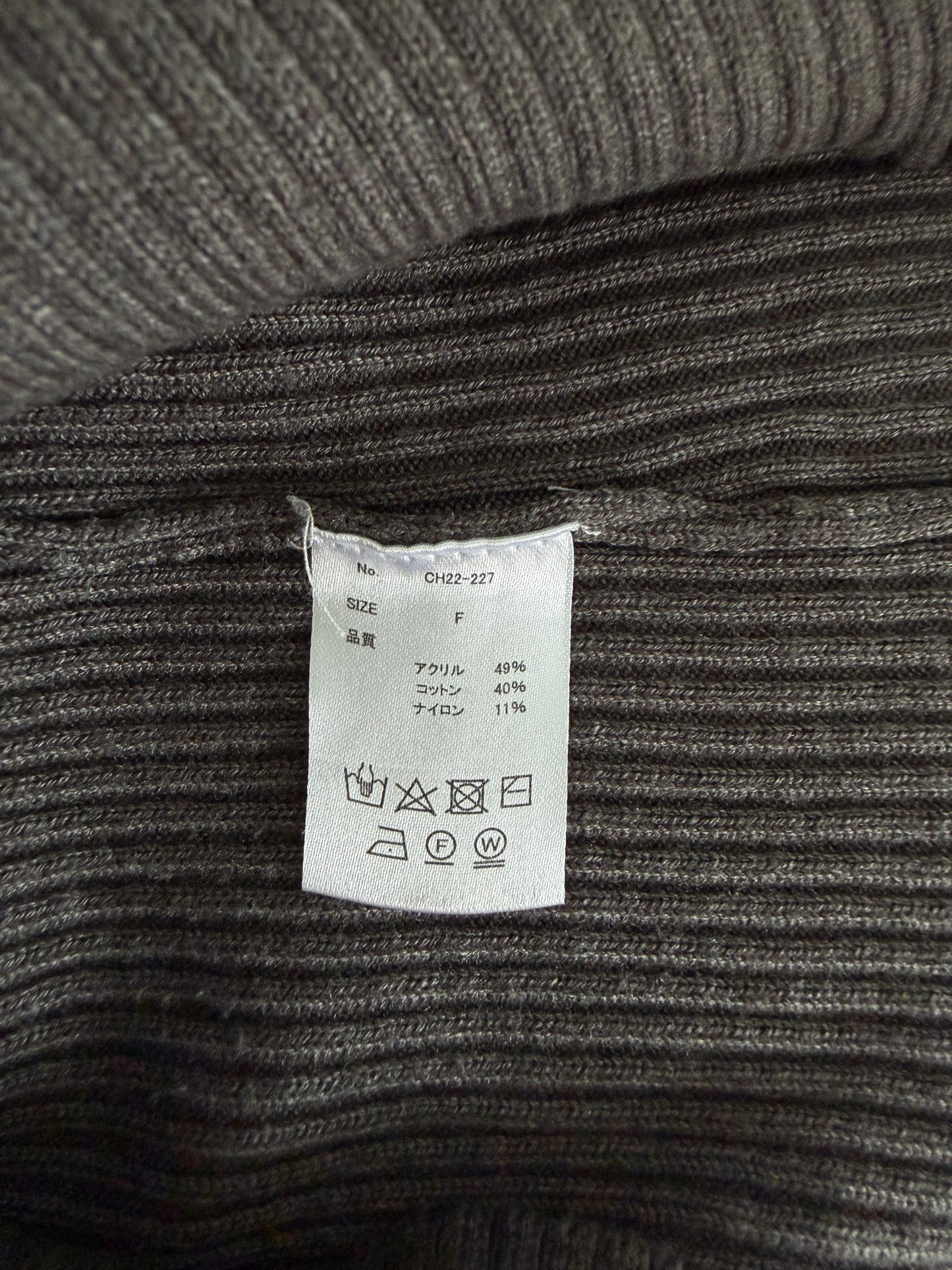 Close-up of a ribbed knit garment in dark gray with a white sewn-in care label visible in the center.