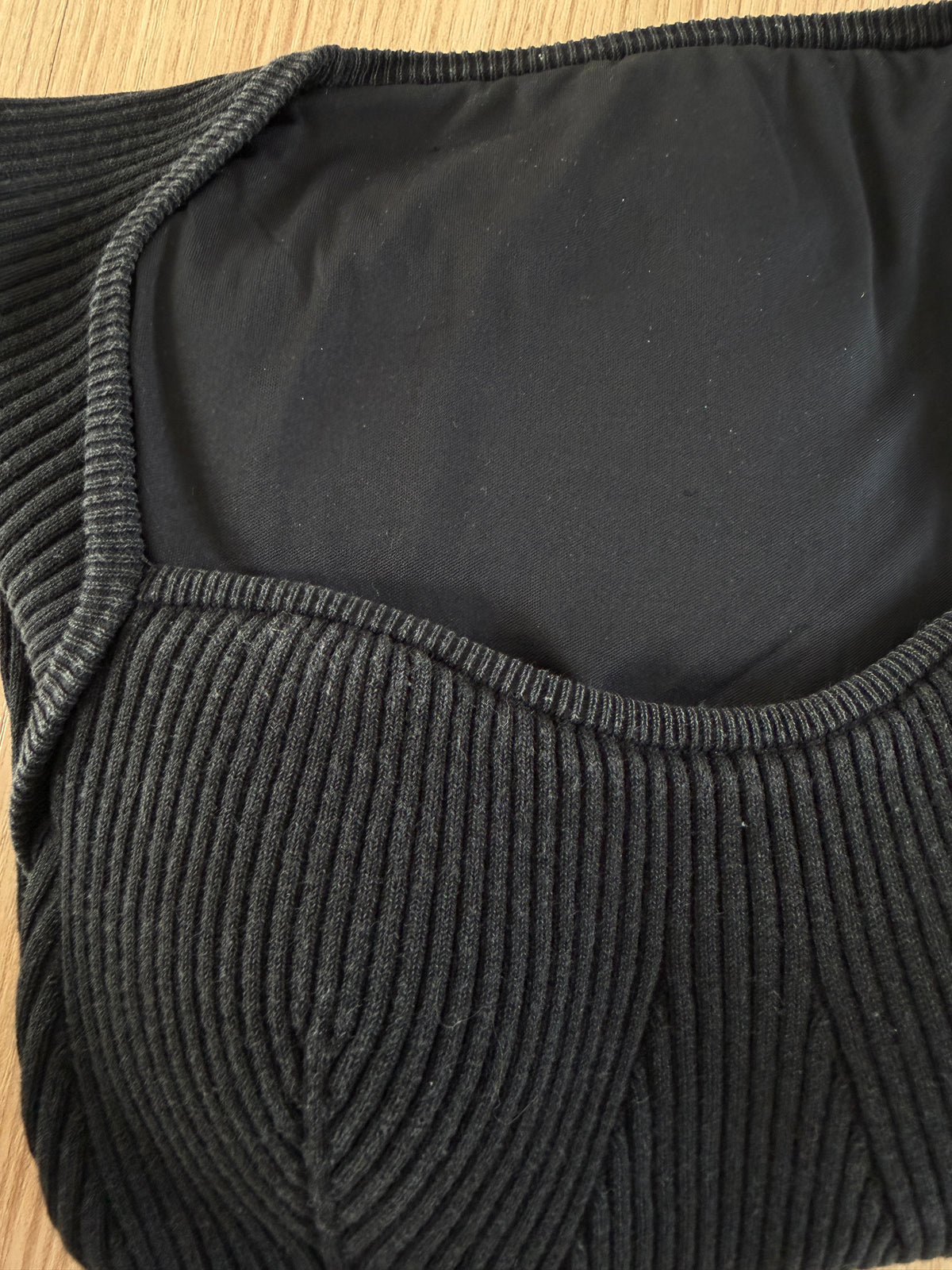 Close-up of a black ribbed knit top, showing the textured corduroy-like fabric and inner lining on a light wood surface.