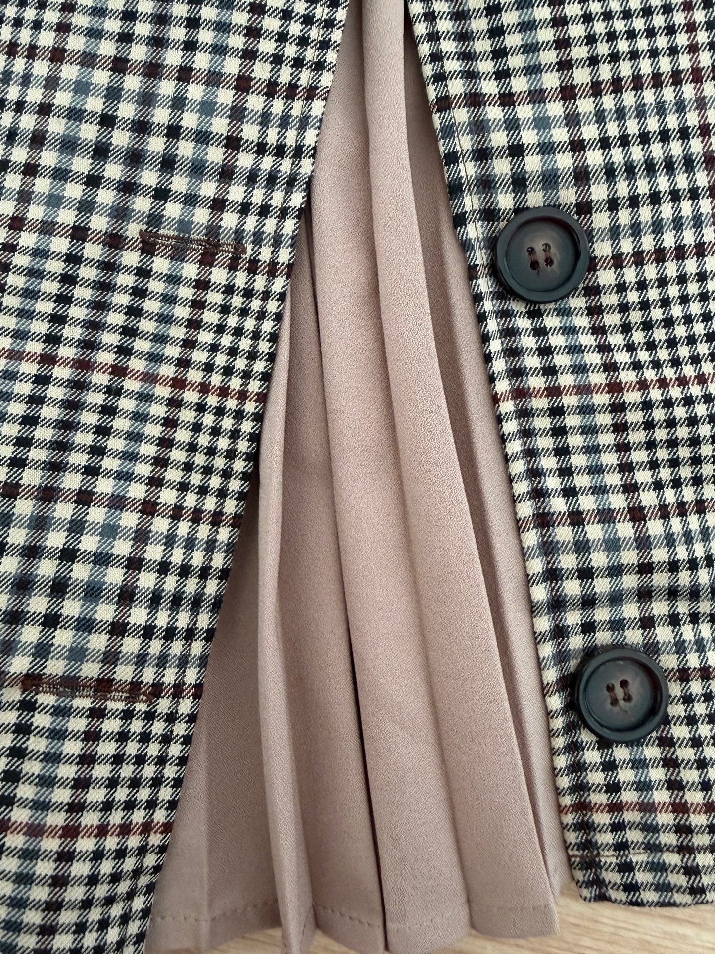 Close-up of a plaid blazer with black buttons, layered over a pleated dusty pink skirt.