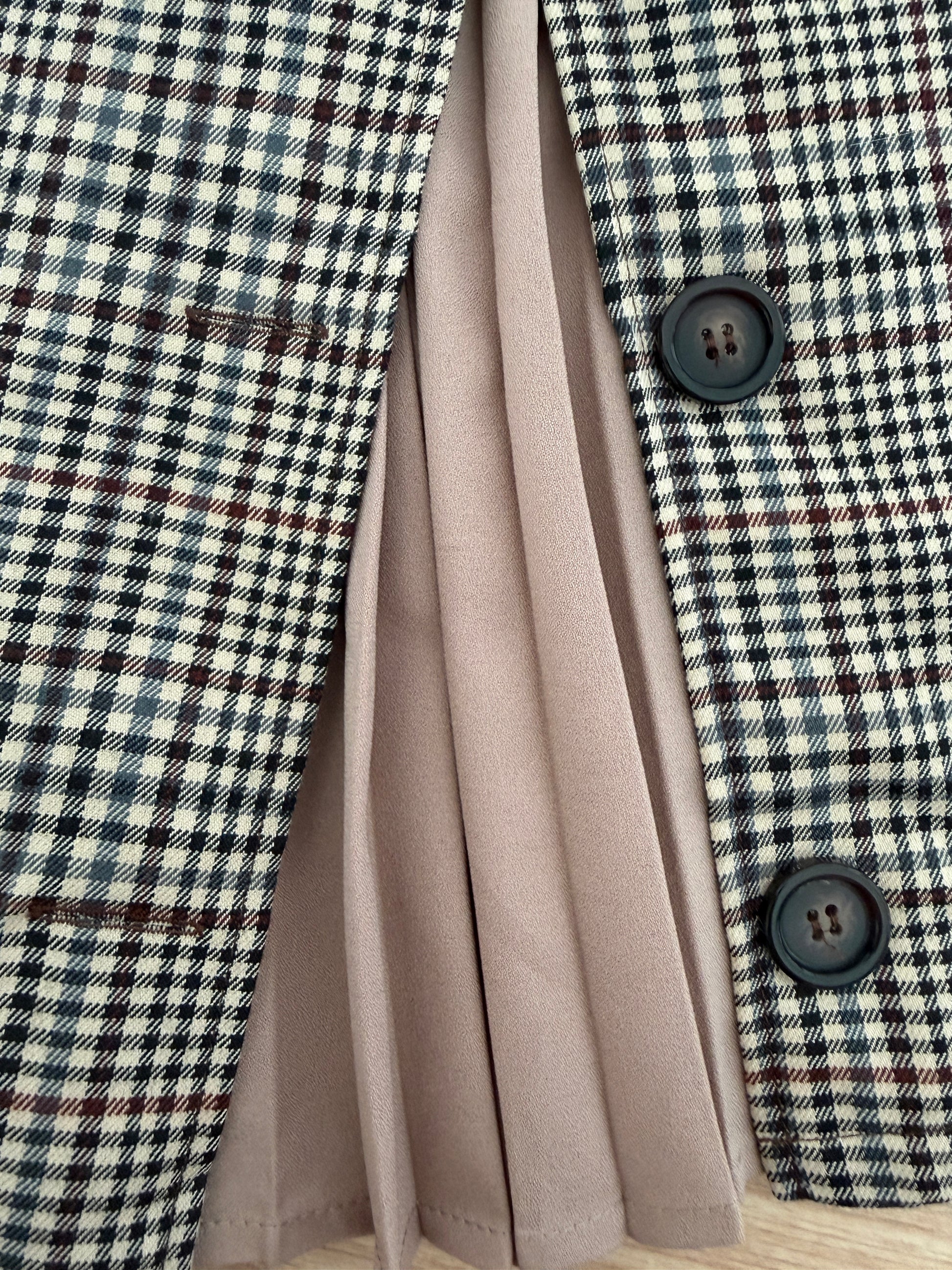 Close-up of a plaid blazer with black buttons, layered over a pleated dusty pink skirt.