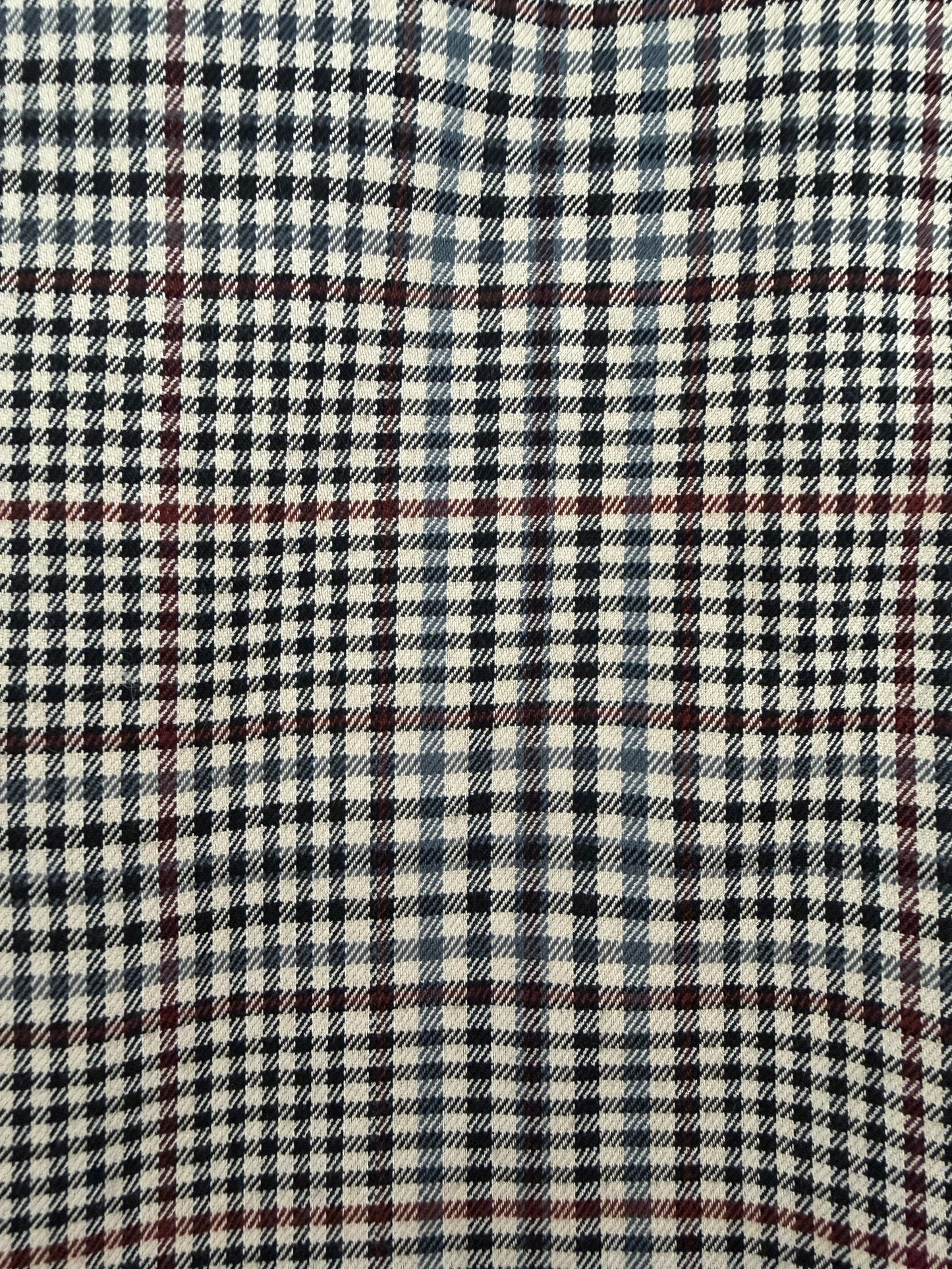A close-up of a plaid fabric pattern with cream, black, navy, and thin red lines.