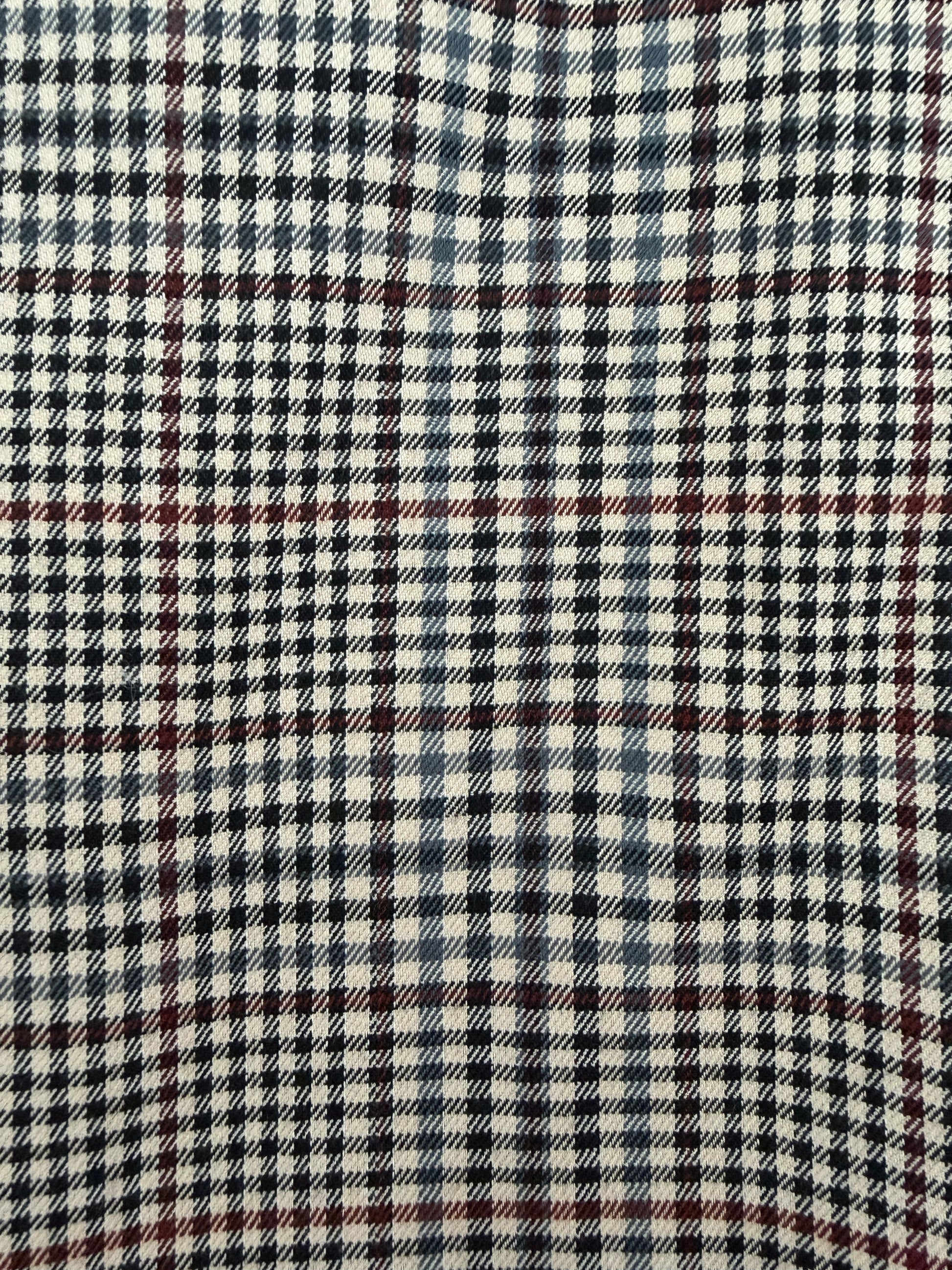 A close-up of a plaid fabric pattern with cream, black, navy, and thin red lines.