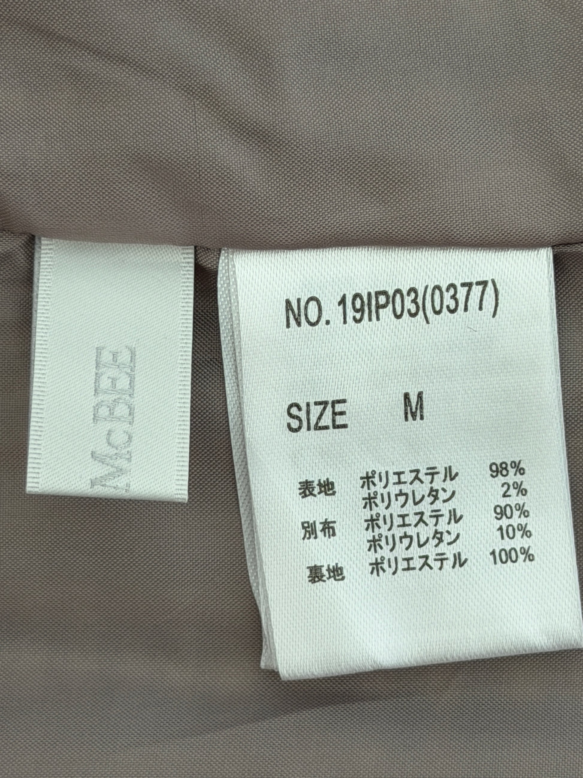 Close-up of a garment's interior labels showing the brand 'M'BBEE' and size 'M' details for a polyester garment.