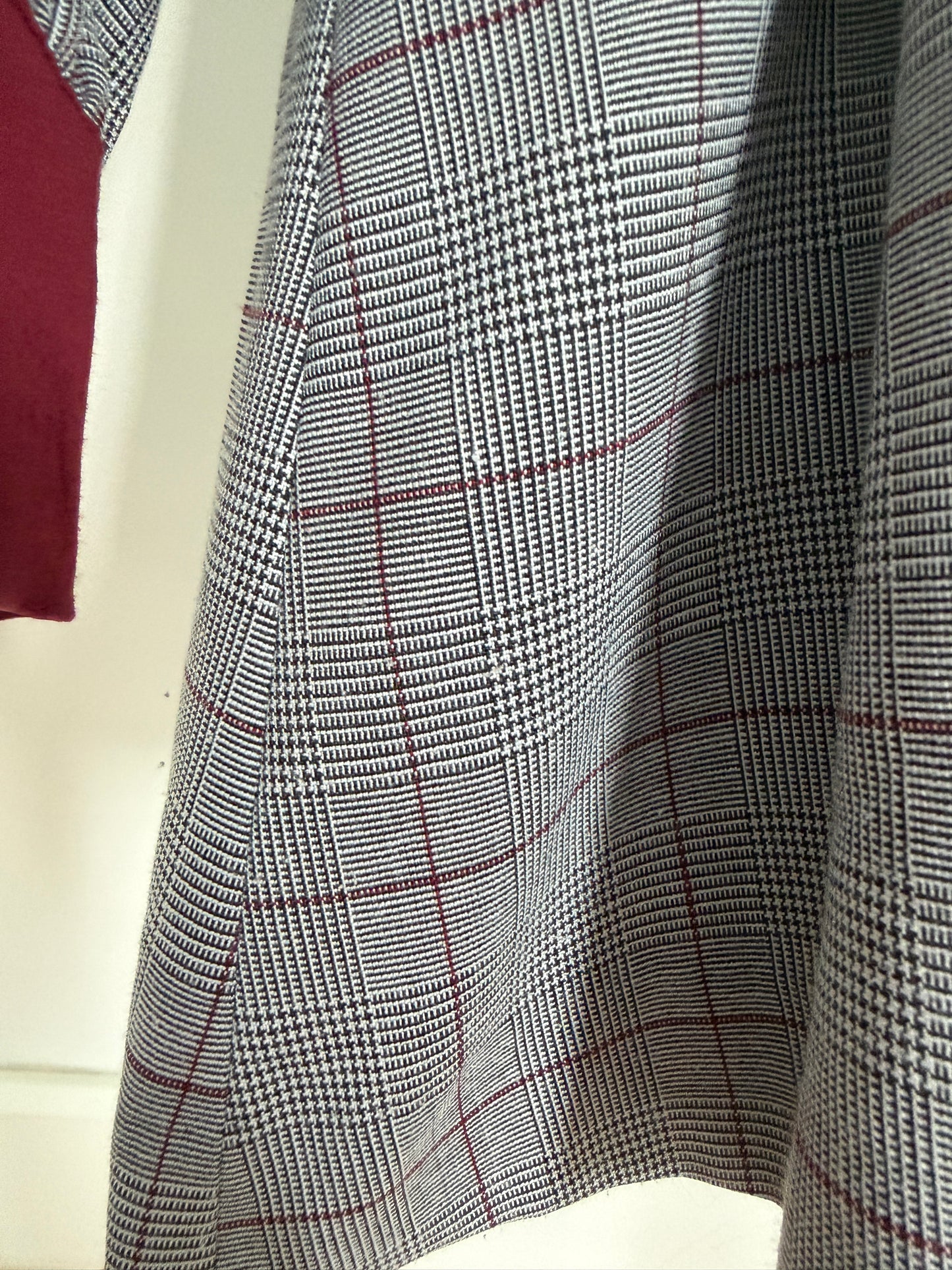 Close-up of a gray and black houndstooth fabric with a thin red windowpane plaid pattern, draped to show its texture and weave.