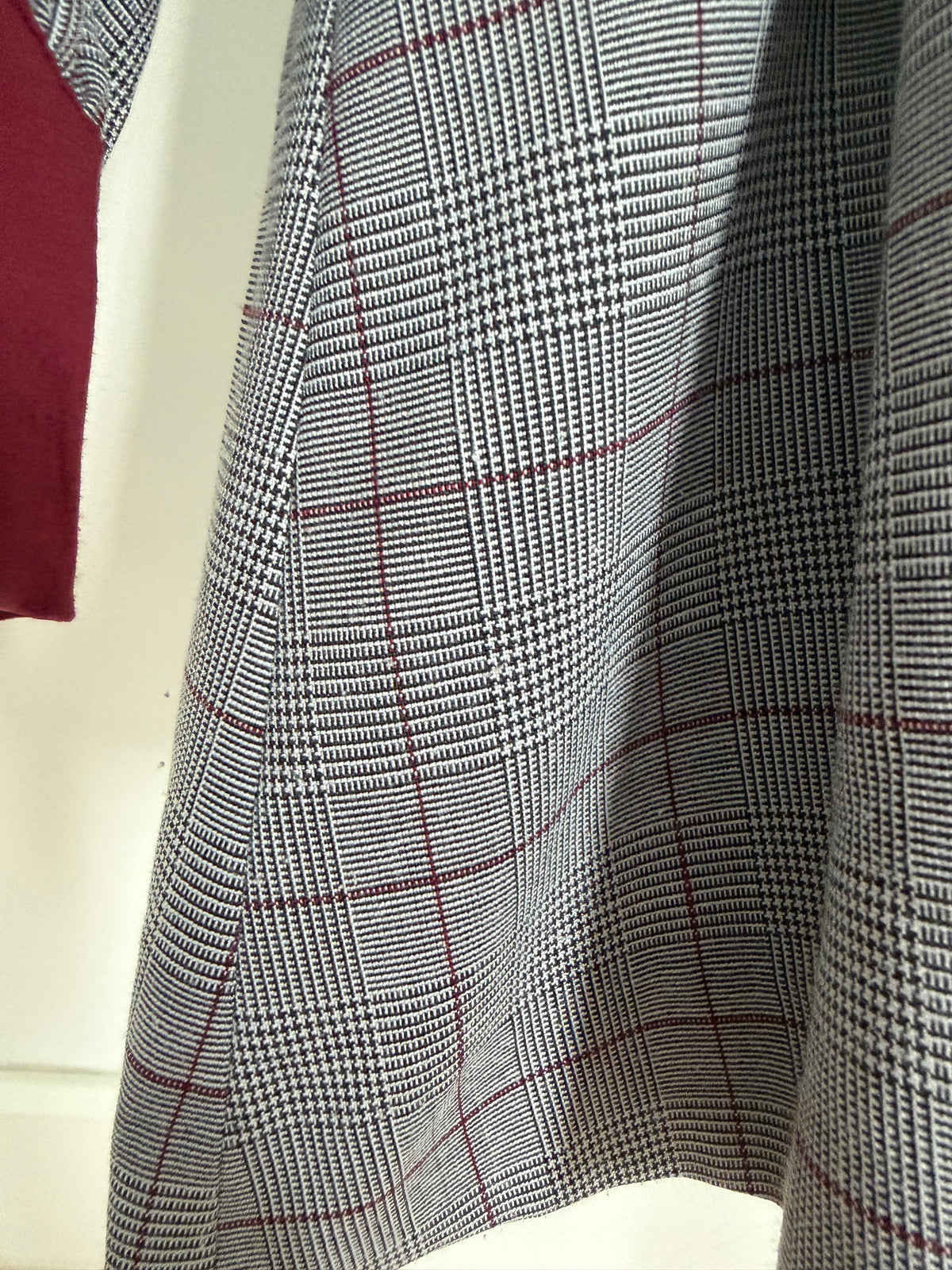 Close-up of a gray and black houndstooth fabric with a thin red windowpane plaid pattern, draped to show its texture and weave.