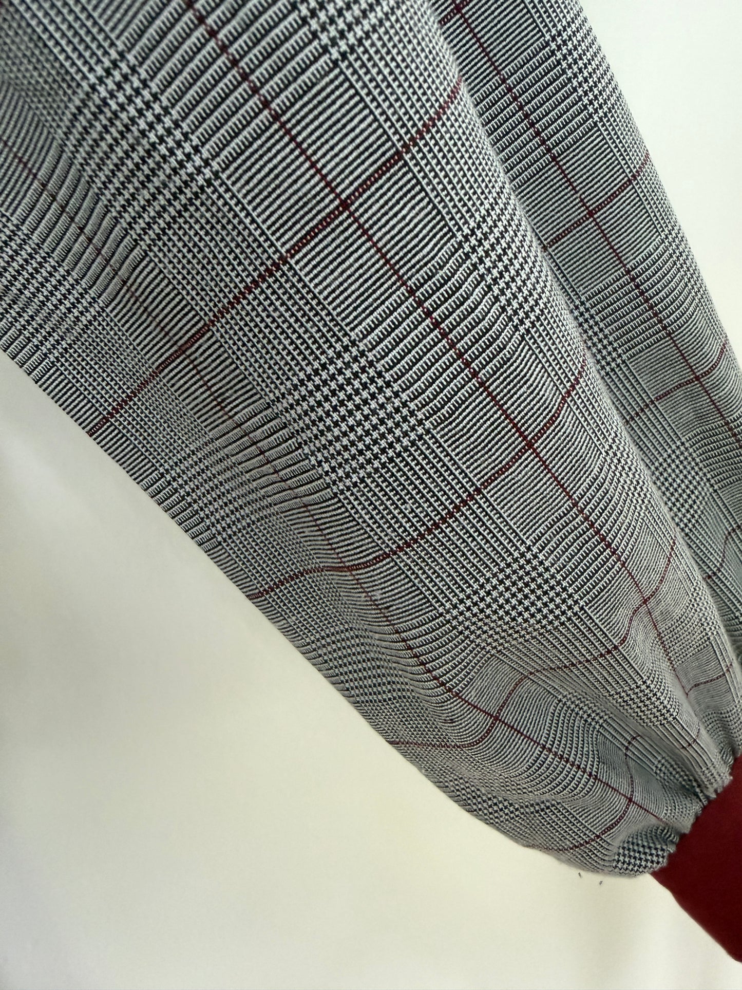 A close-up of a gray and white plaid fabric with thin red windowpane lines, draped diagonally against a plain off-white background.