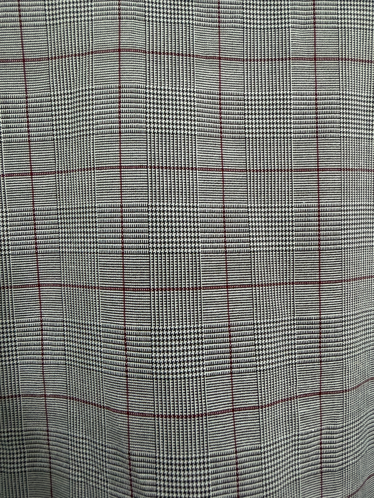 A close-up of a plaid fabric pattern featuring a black and white houndstooth weave with thin red windowpane lines.