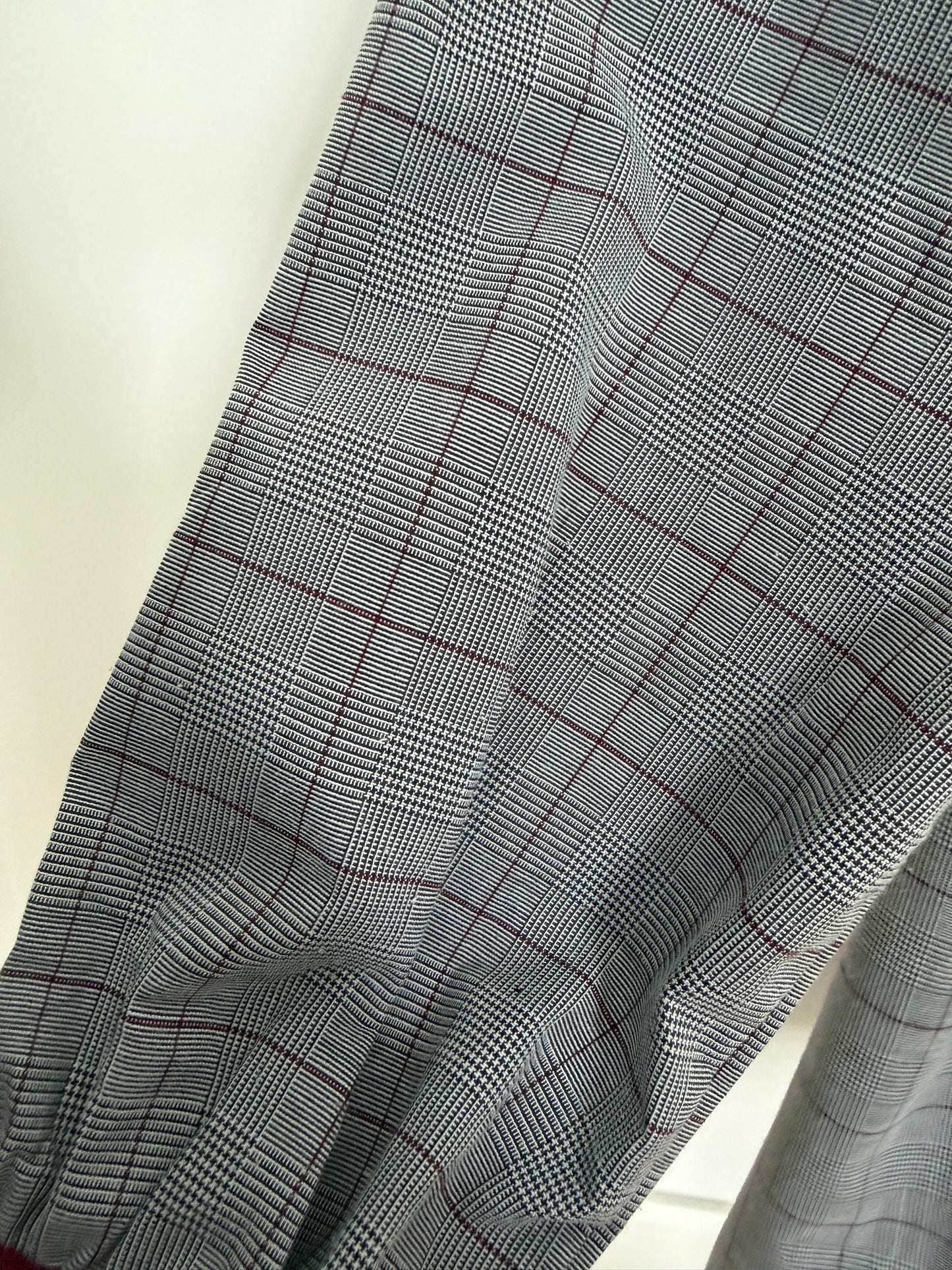 A close-up of a gray and black plaid fabric with thin red grid lines, draped diagonally across the frame.
