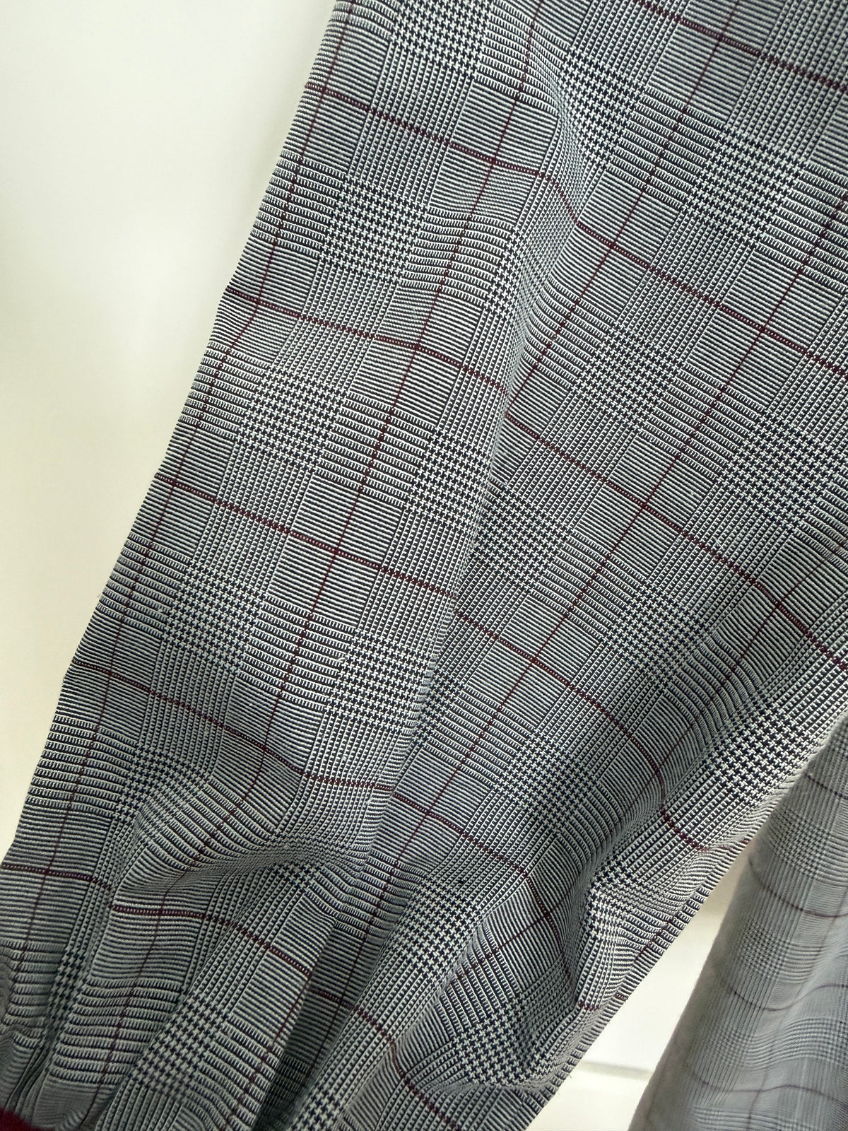 A close-up of a gray and black plaid fabric with thin red grid lines, draped diagonally across the frame.