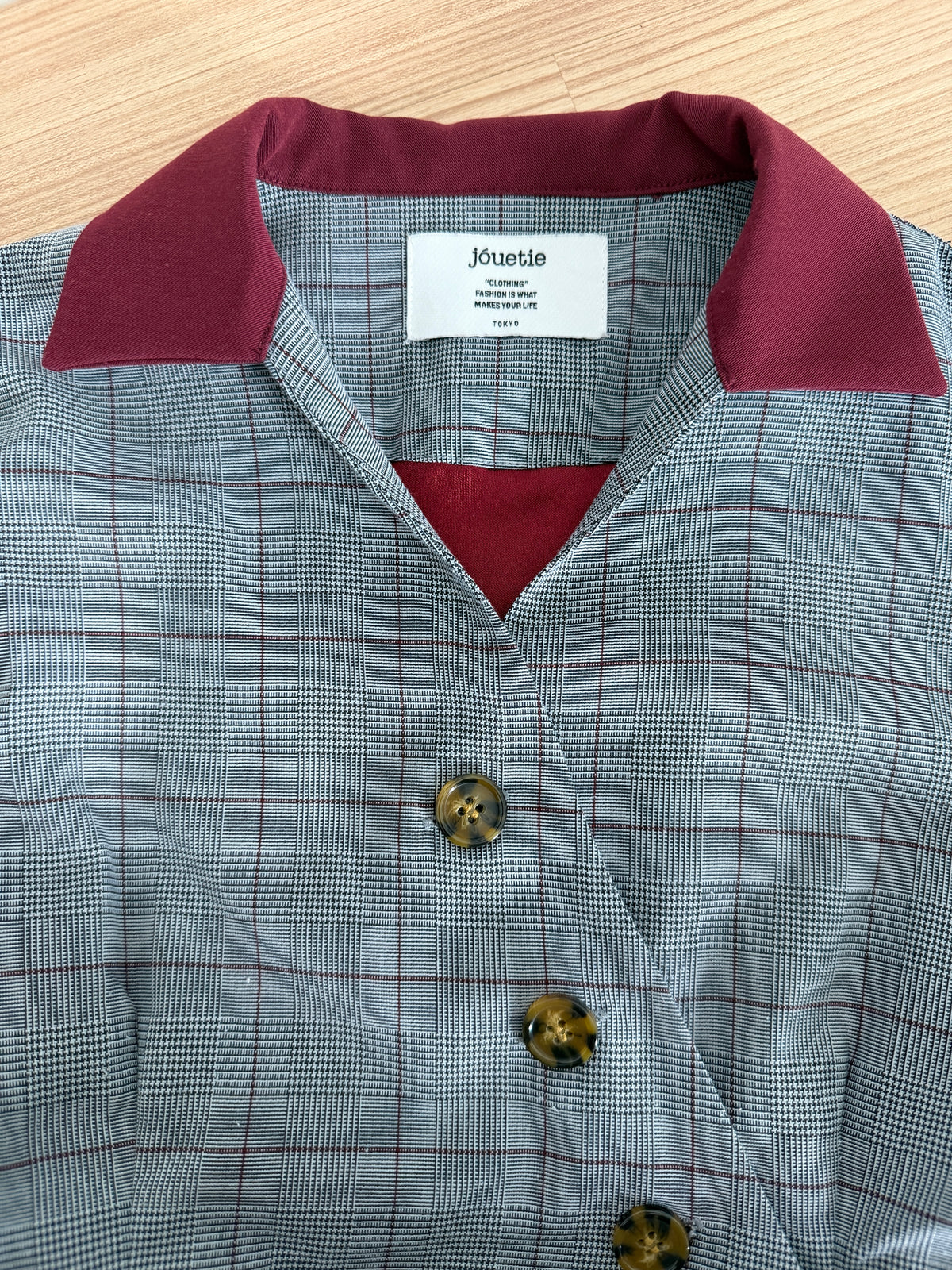 A close-up of a Jueblie shirt featuring a gray and white windowpane plaid body with a contrasting deep burgundy collar and matching inner plaid lining.