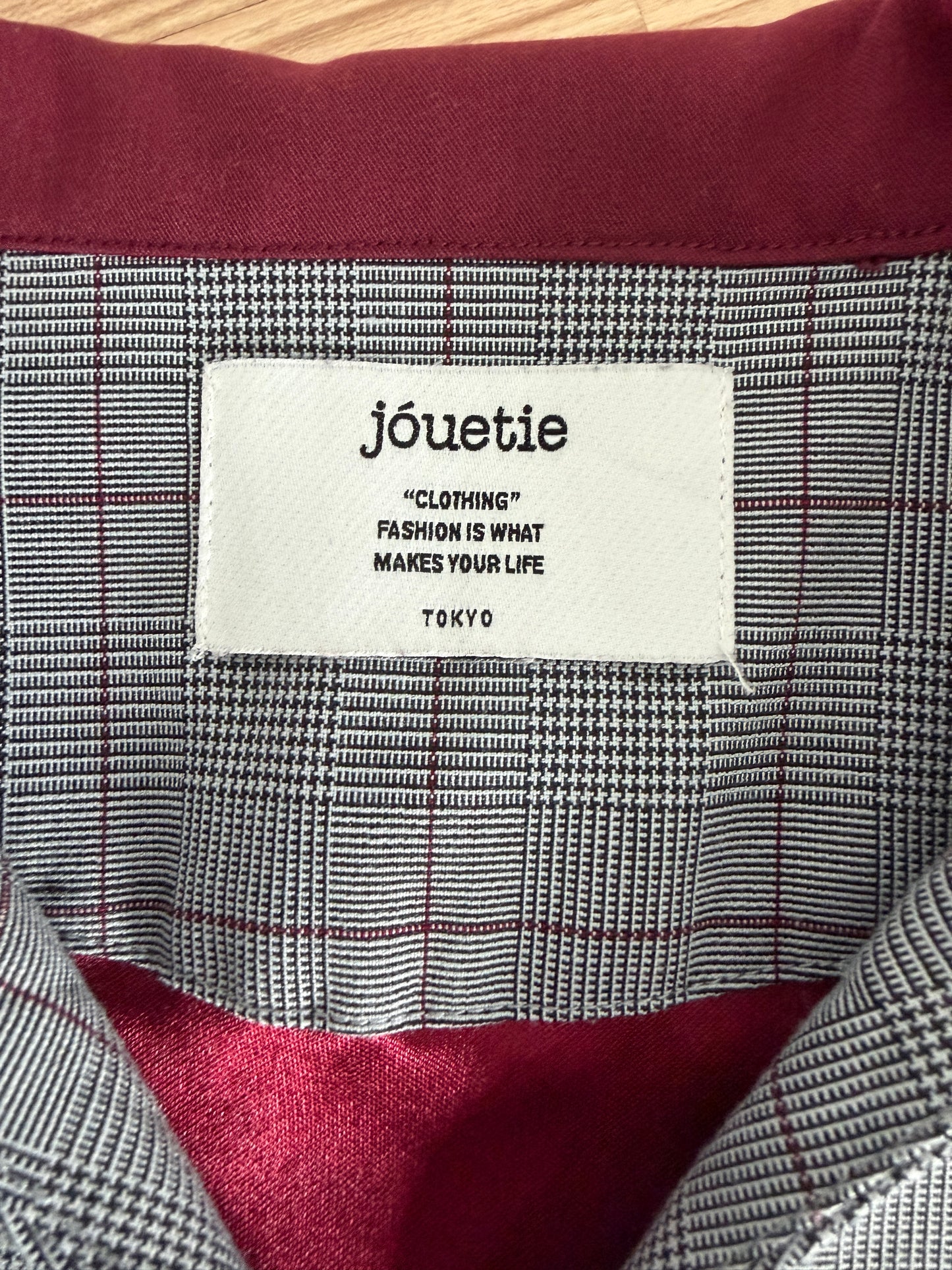 Close-up of the inside collar of a plaid shirt with a white brand label reading 'jôuetie' and 'TOKYO' on a burgundy lining.