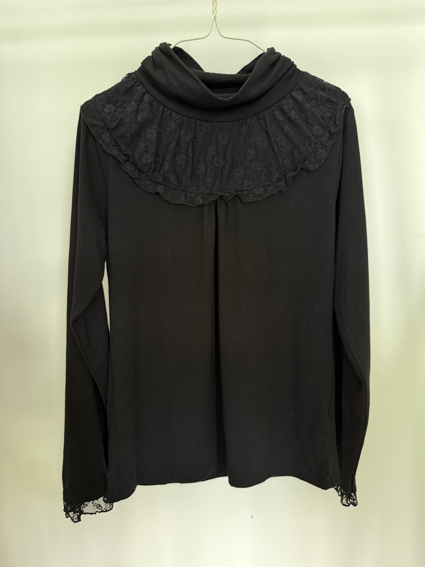 A black long-sleeve turtleneck top with lace trim at the cuffs, hanging on a white hanger against a plain off-white background.