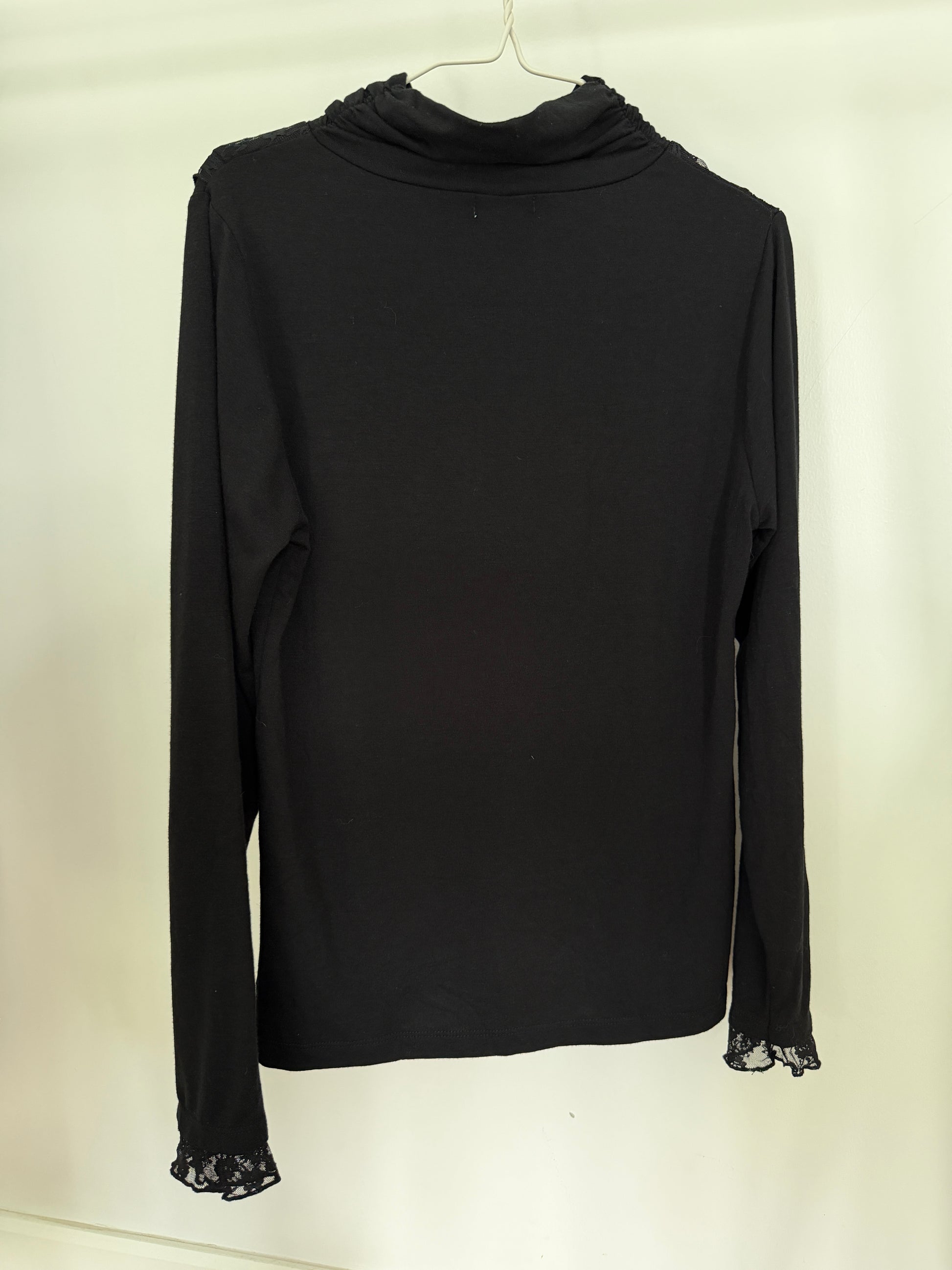A black long-sleeve turtleneck top with lace trim at the cuffs, hanging on a white hanger against a plain off-white background.